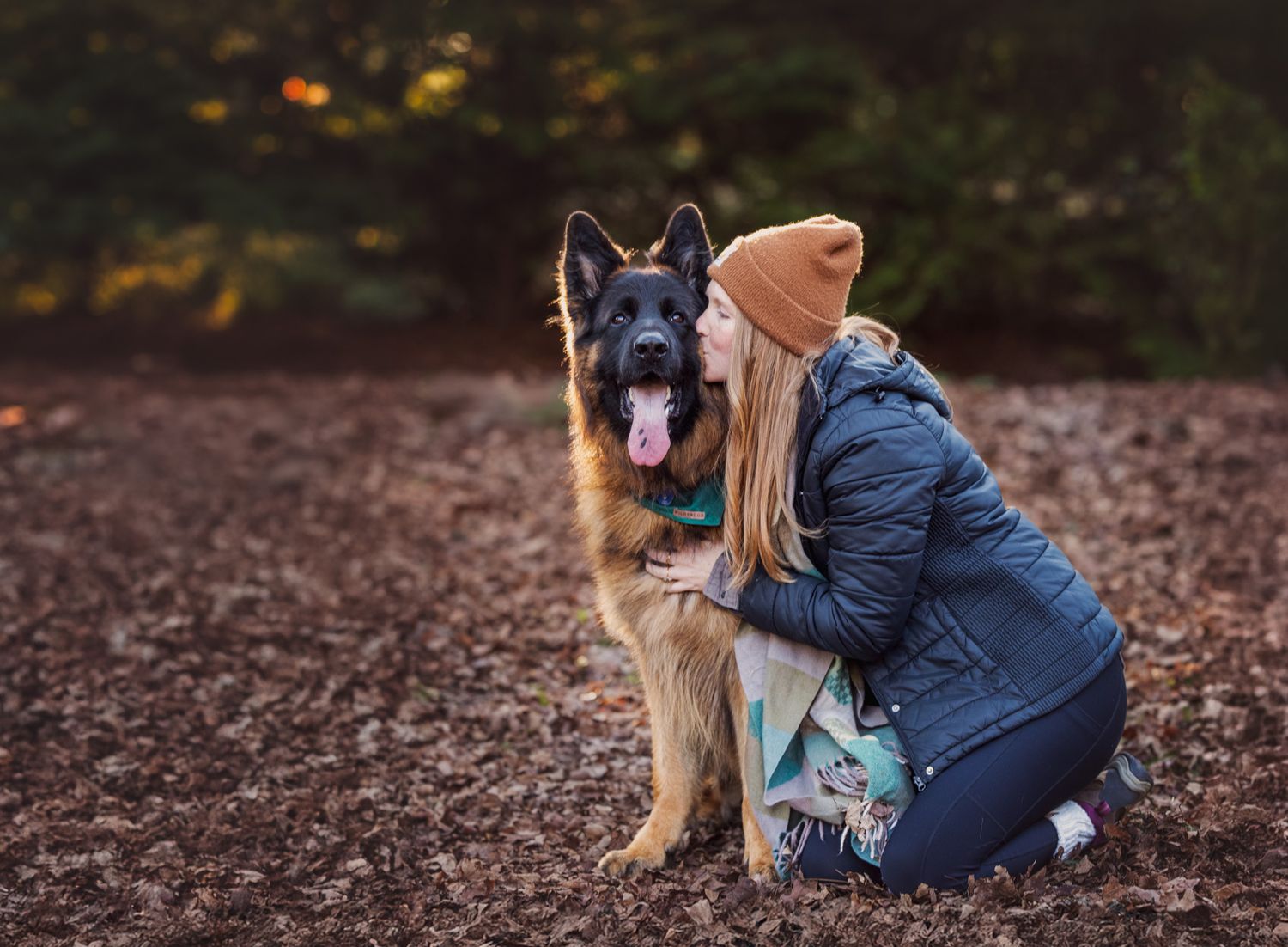 Woman kneeling leans over to kiss German Shepard dog amongst leaves in winter at Knoxville Botanical Gardens in Knoxville TN