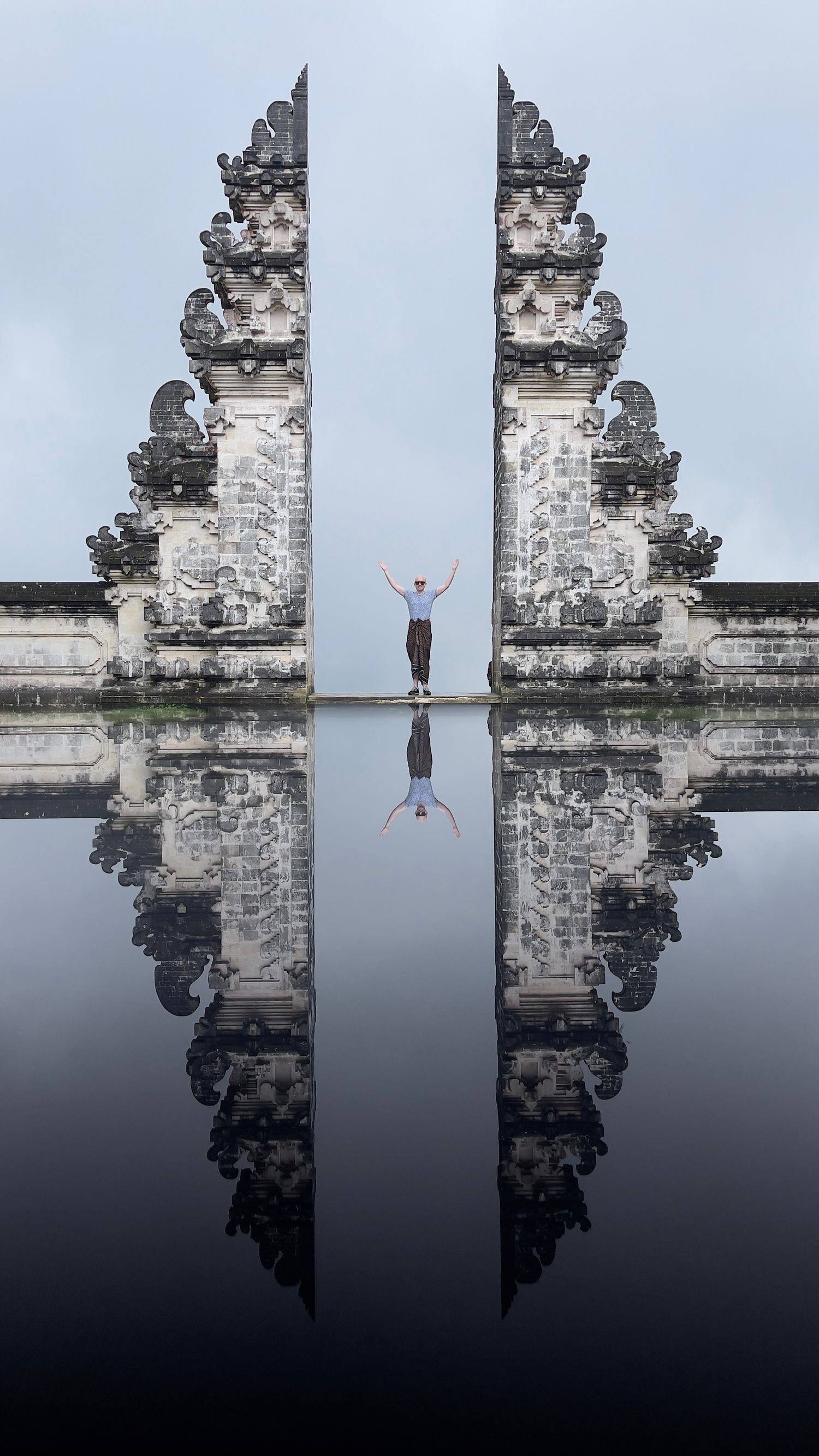Reflective surface creates symmetrical mirror image of ancient Balinese temple gates against dark water.