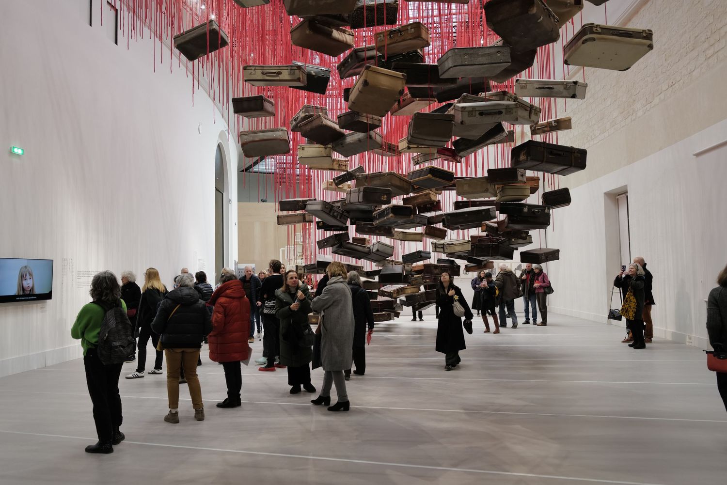 Modern art installation with dark geometric shapes suspended from ceiling in white gallery space.