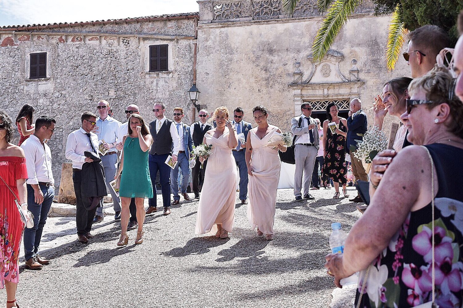 Wedding party and guests gathered in a historic stone courtyard for outdoor celebration.