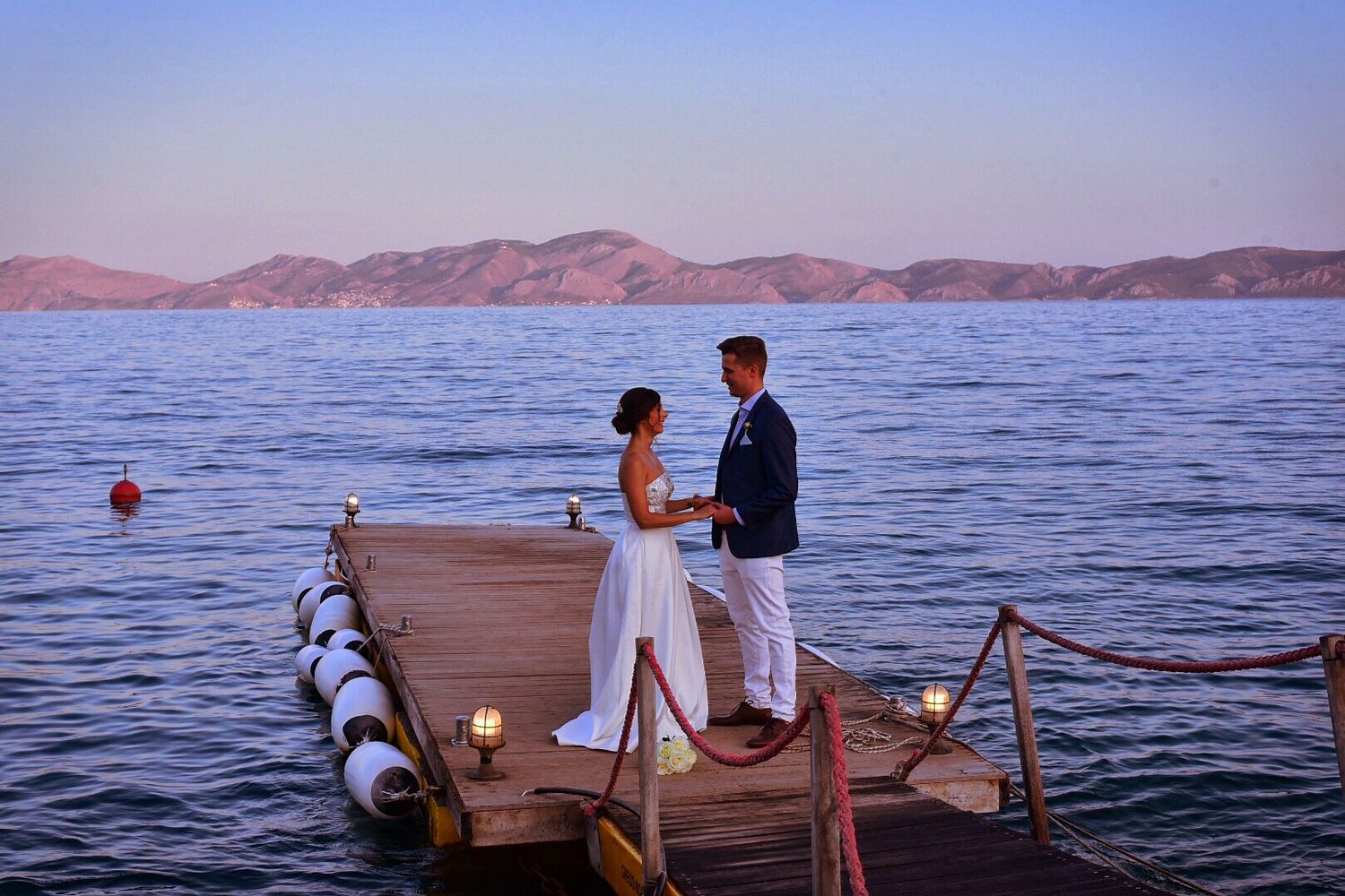 Romantic scene of a couple standing on a wooden dock at sunset with mountains in the background.