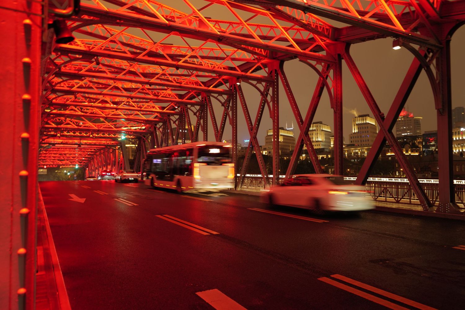 Red-lit Waibaidu Bridge in Shanghai with cars passing through at night.