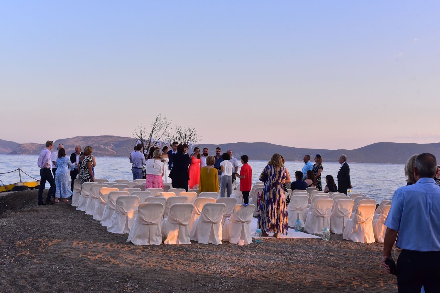 Evening wedding ceremony setup with white-covered chairs and glowing lanterns by the water.