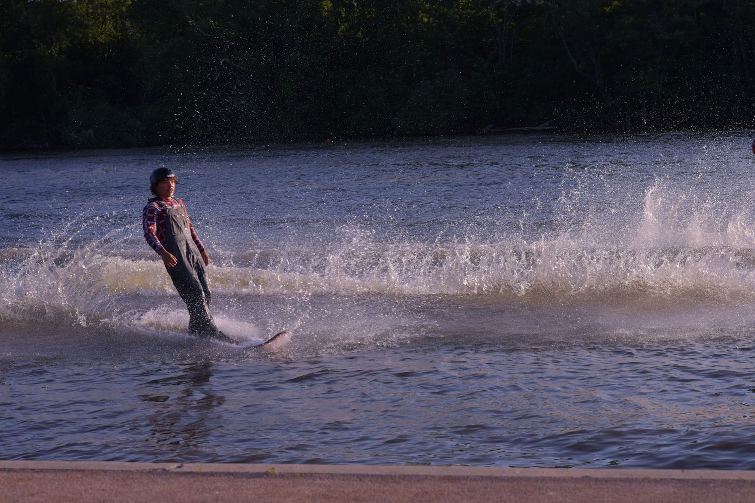 A water skier glides across a lake creating a dramatic splash of water at sunset.