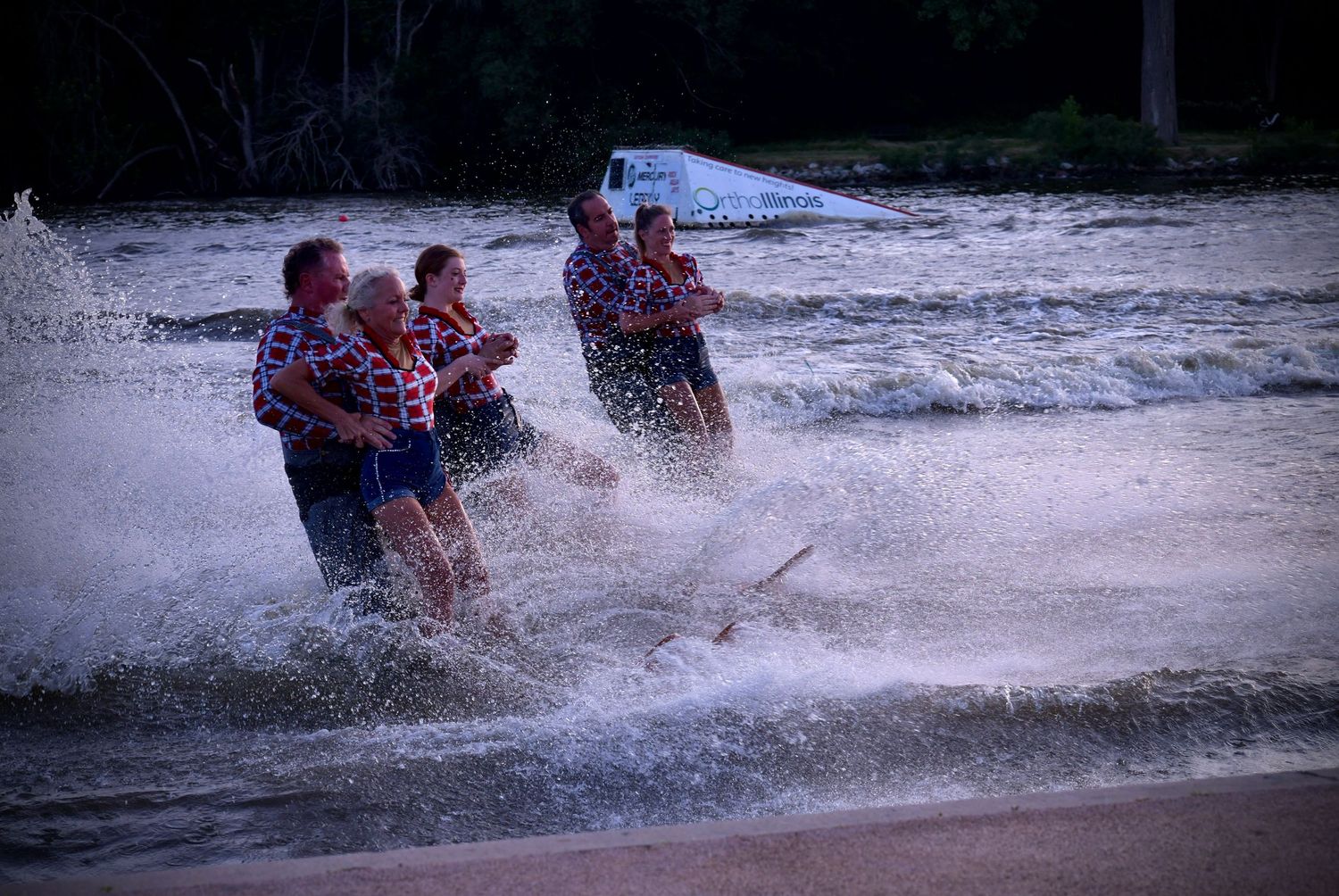 Group waterskiing through splashing waves while being pulled by a boat during an action-packed water sports session.