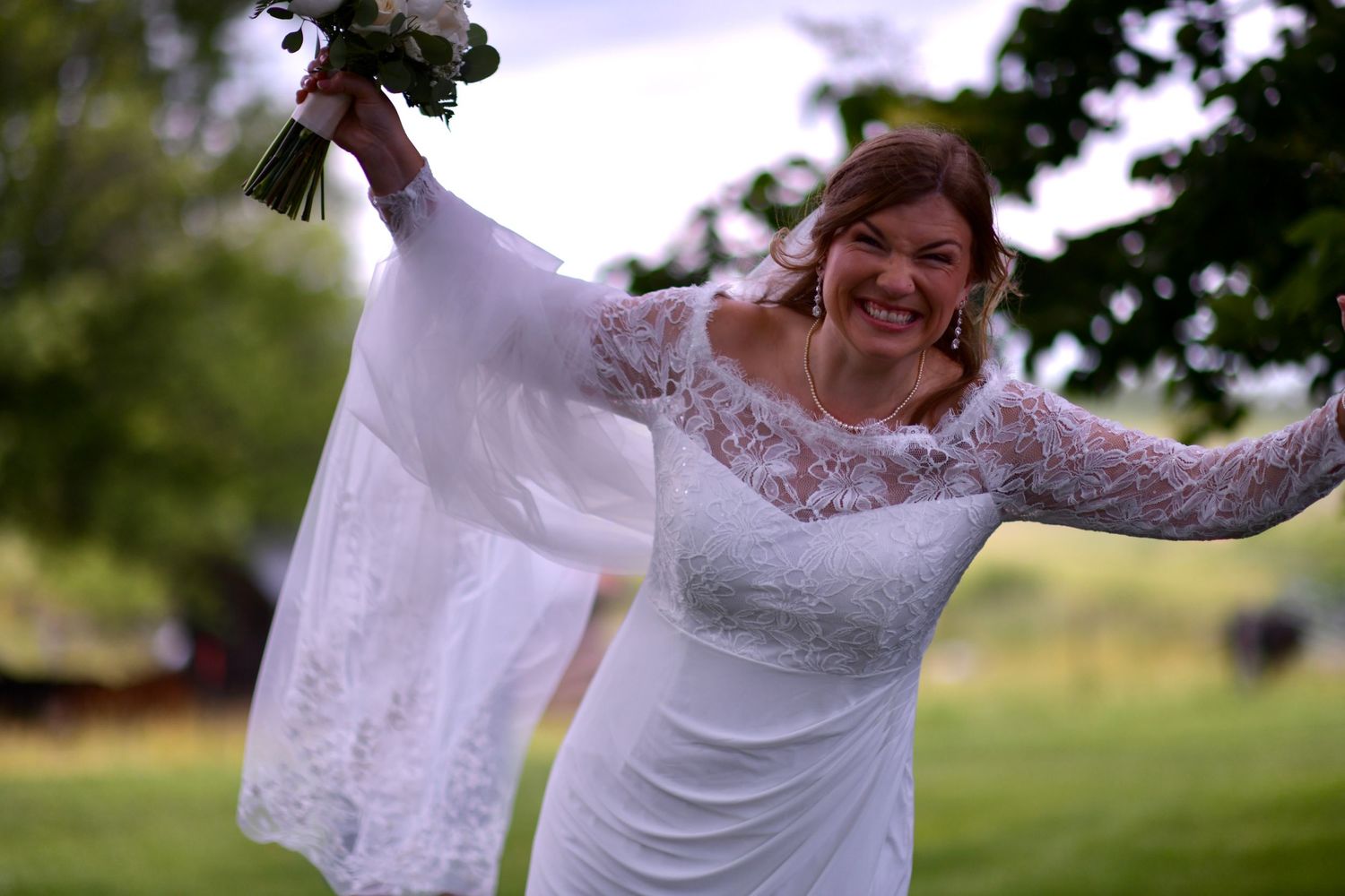 Bride in lace gown twirls joyfully outdoors showing off long flowing sleeves.