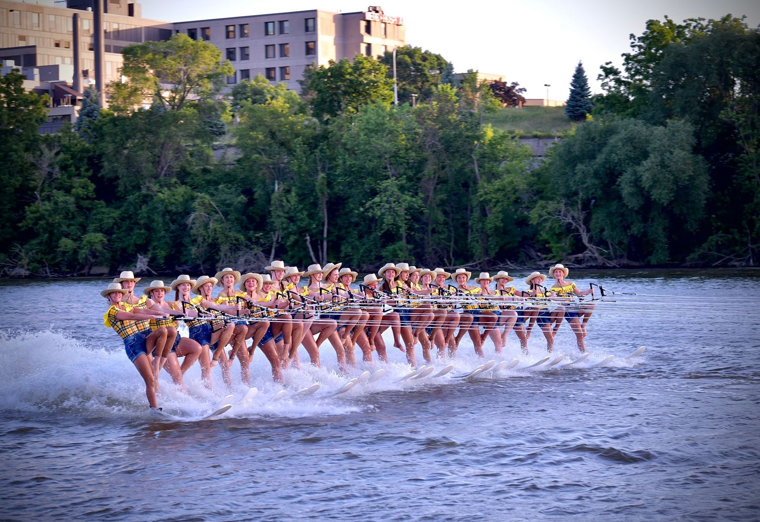 A line of water skiers performing in formation on a lake during sunset creates a stunning display of synchronized skiing.