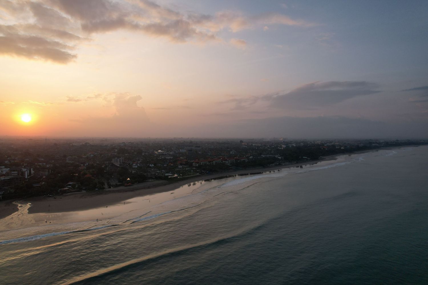 Aerial view of a coastal sunset with golden light illuminating the shoreline.