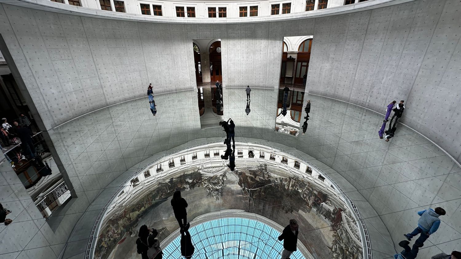 Minimalist circular gallery space with reflective floor and visitors viewing exhibits.