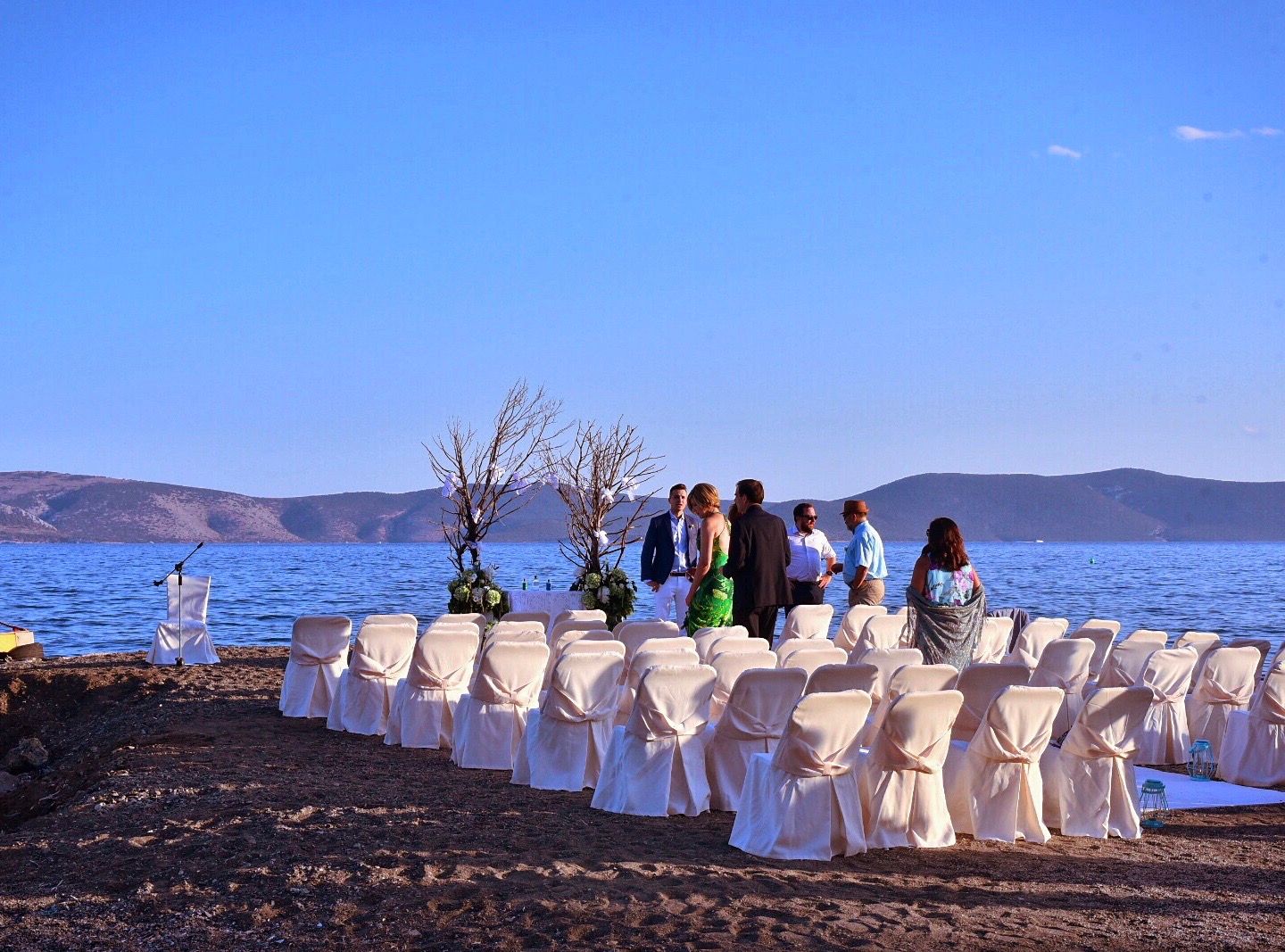 Seaside wedding setup with white-covered chairs facing ceremony site overlooking blue waters.