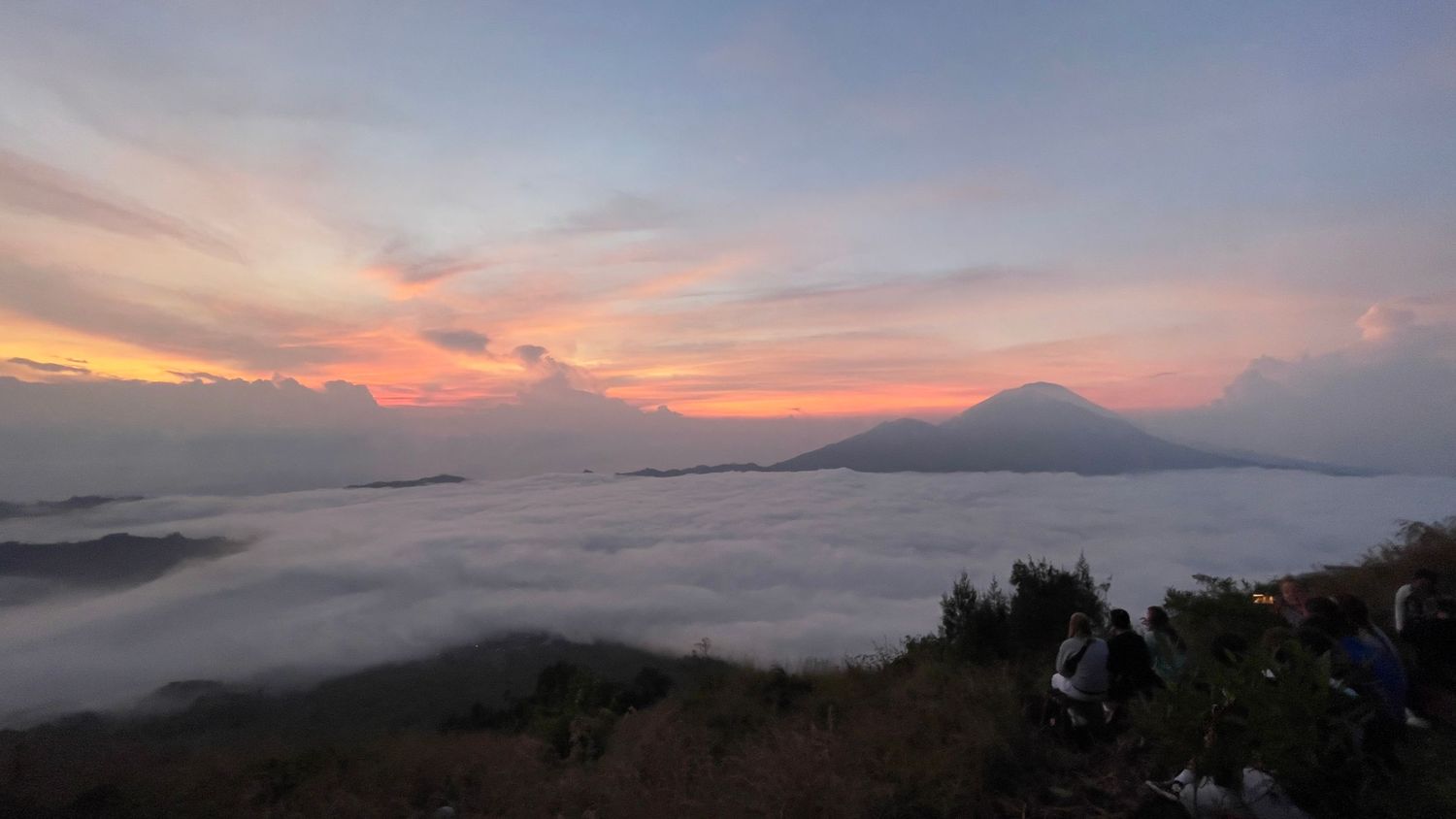 Mountain peak emerging above sea of clouds during colorful sunrise in Indonesia.