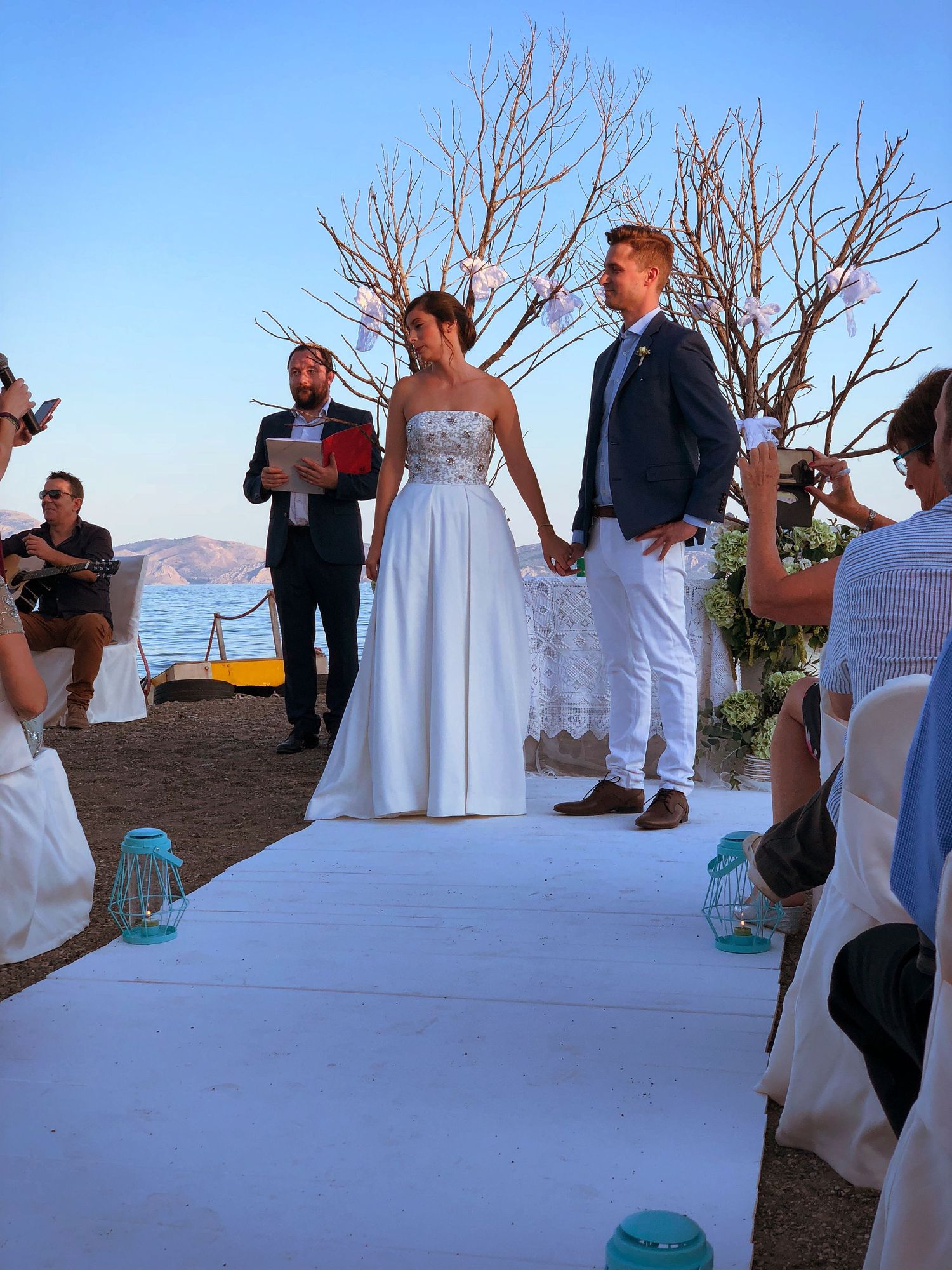 Wedding ceremony on coastal cliff with couple holding hands on white aisle runner.