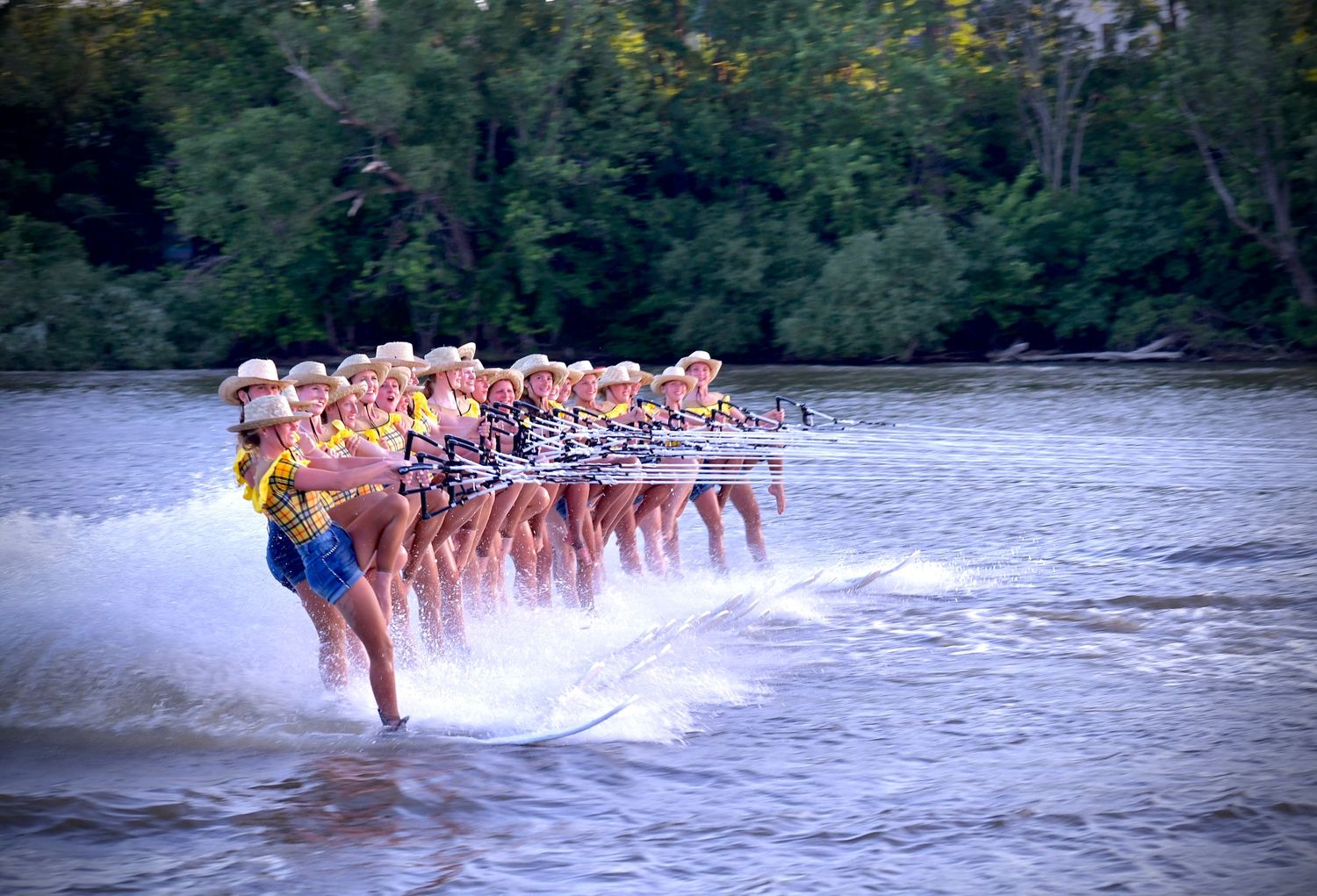 Water ski team performs synchronized leg lift while gliding across lake surface in matching pink uniforms.