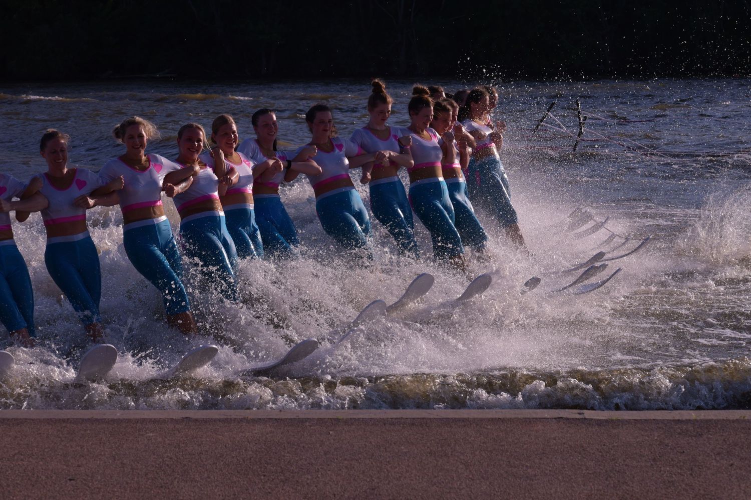 A water skiing team performs a synchronized line formation creating dramatic splashes on the water's surface.