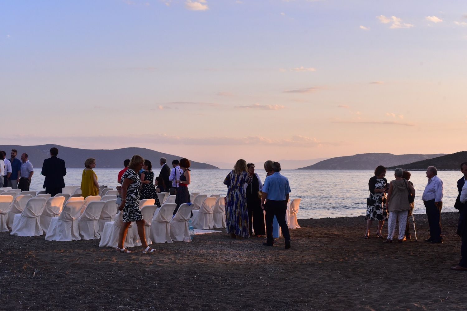 Wedding guests gathered on coastal cliff overlooking ocean and mountains during sunset ceremony.
