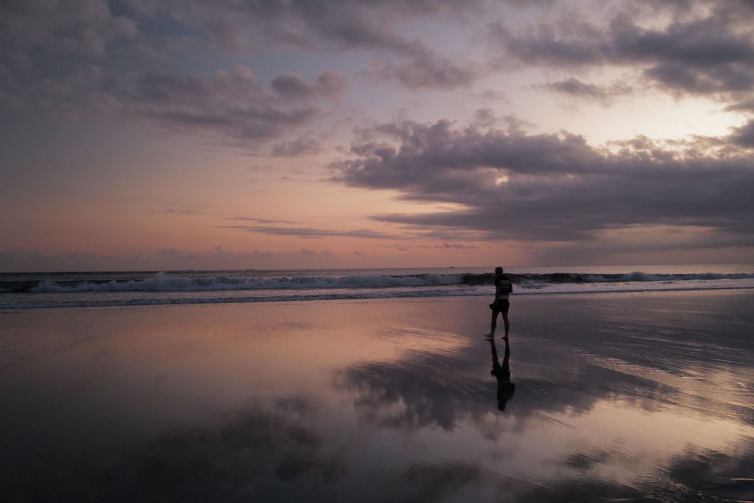 Stunning coastal sunset with silhouetted figures walking along a reflective beach at dusk.