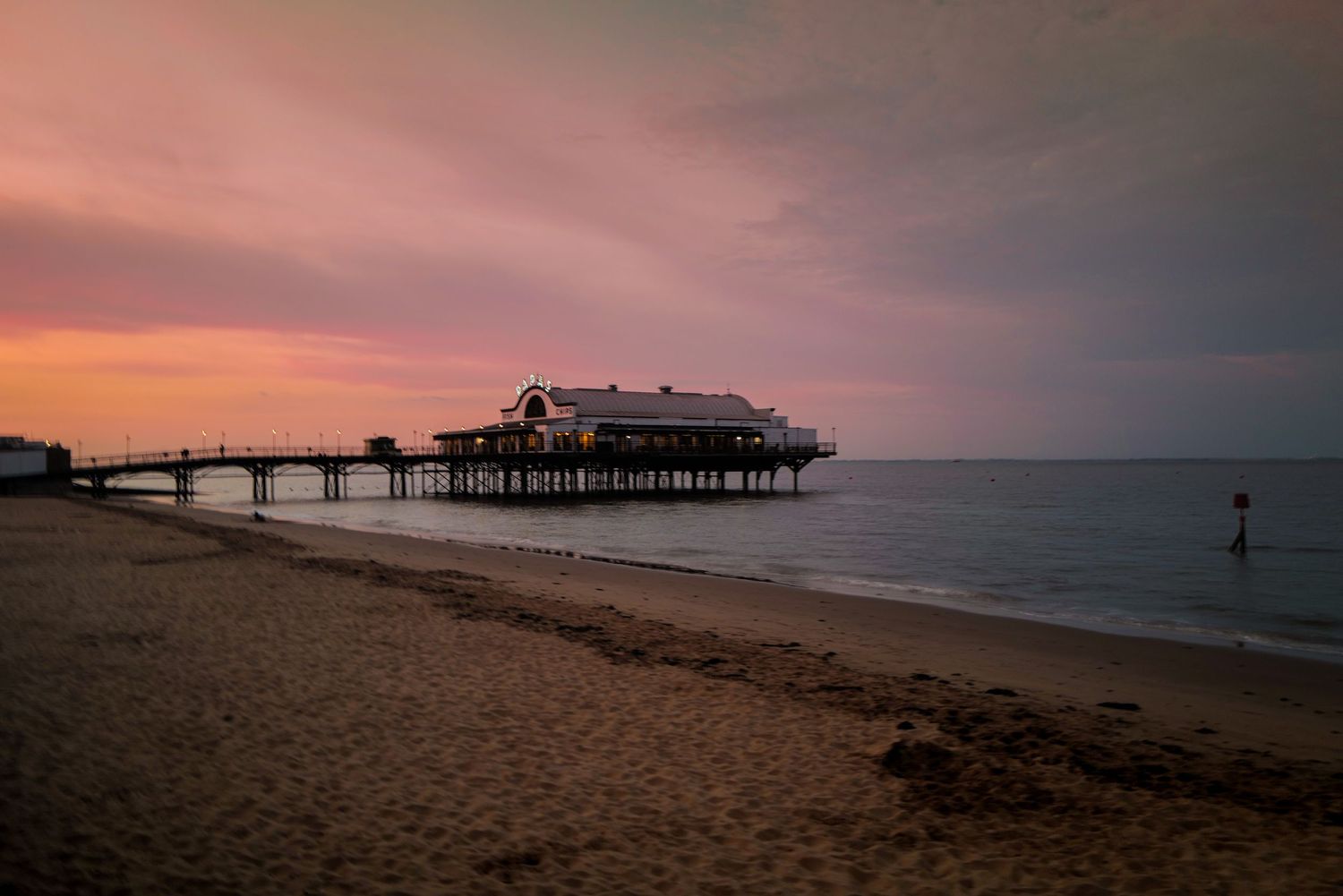 Brighton Pier silhouetted against a dramatic pink sunset sky over the beach in England.