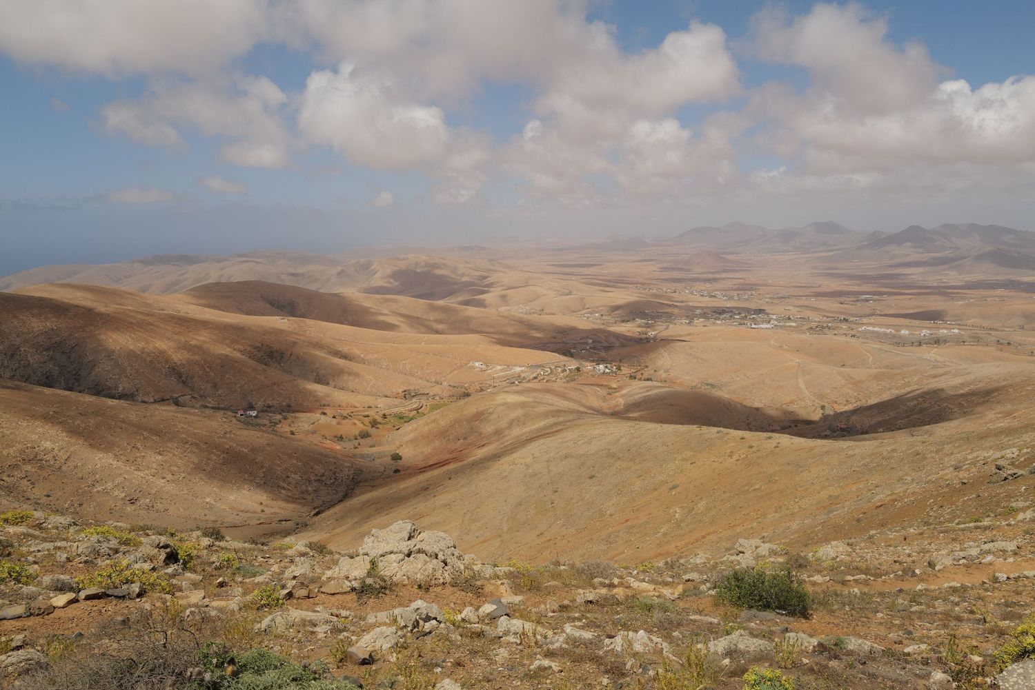 Expansive desert landscape with rolling brown hills stretching to the horizon under a cloudy sky.