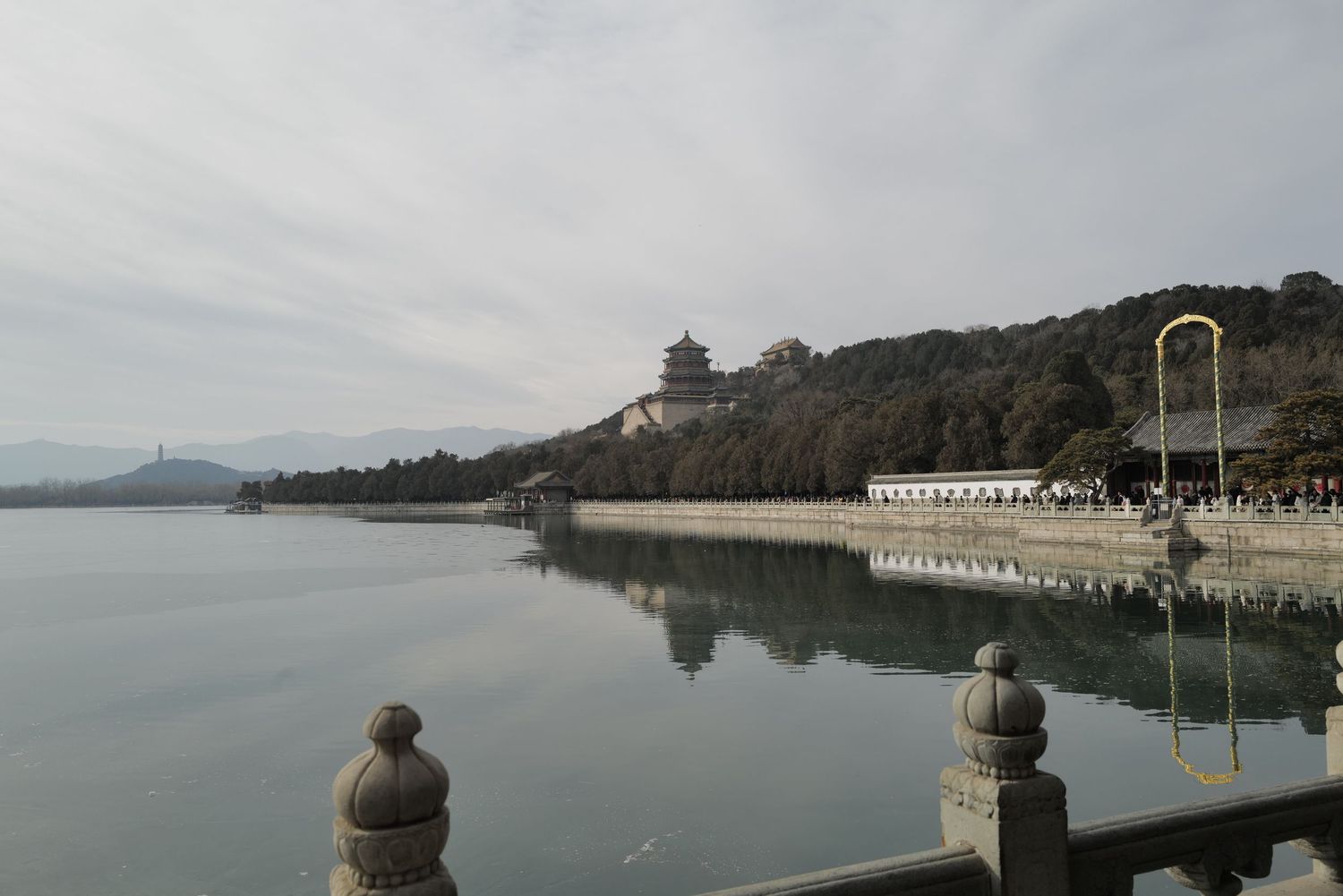 Serene lakeside view with stone railings and a temple complex visible on the hillside.