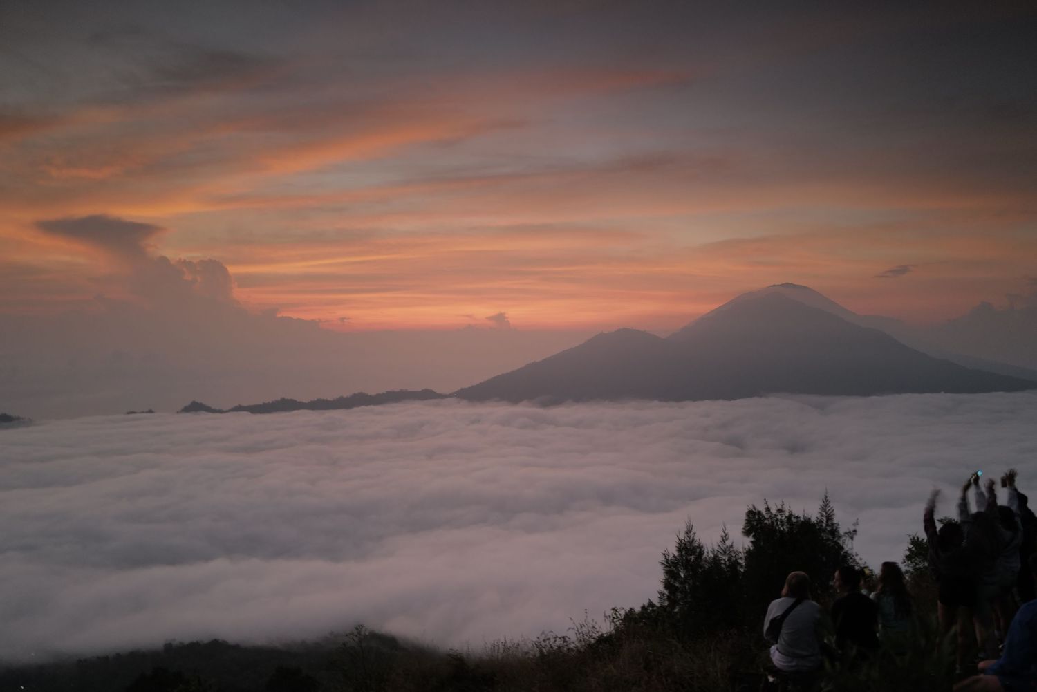 Misty mountain landscape at sunrise with sea of clouds beneath volcanic peaks.