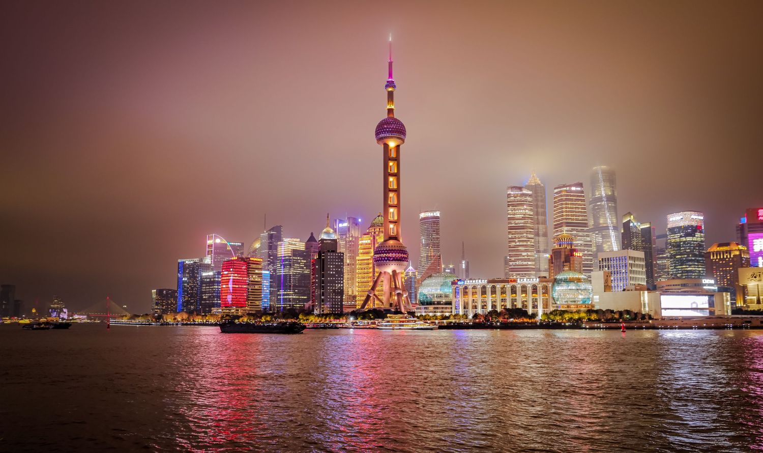 Shanghai's illuminated Pudong skyline with Oriental Pearl Tower reflected in Huangpu River at night.