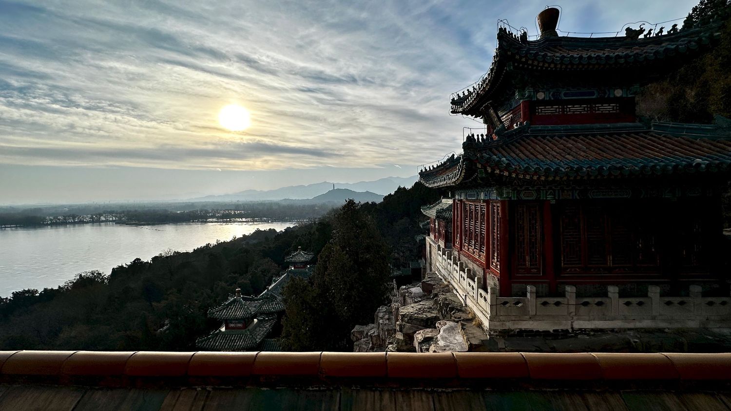Silhouetted Asian temple buildings against dramatic sunset sky with clouds.