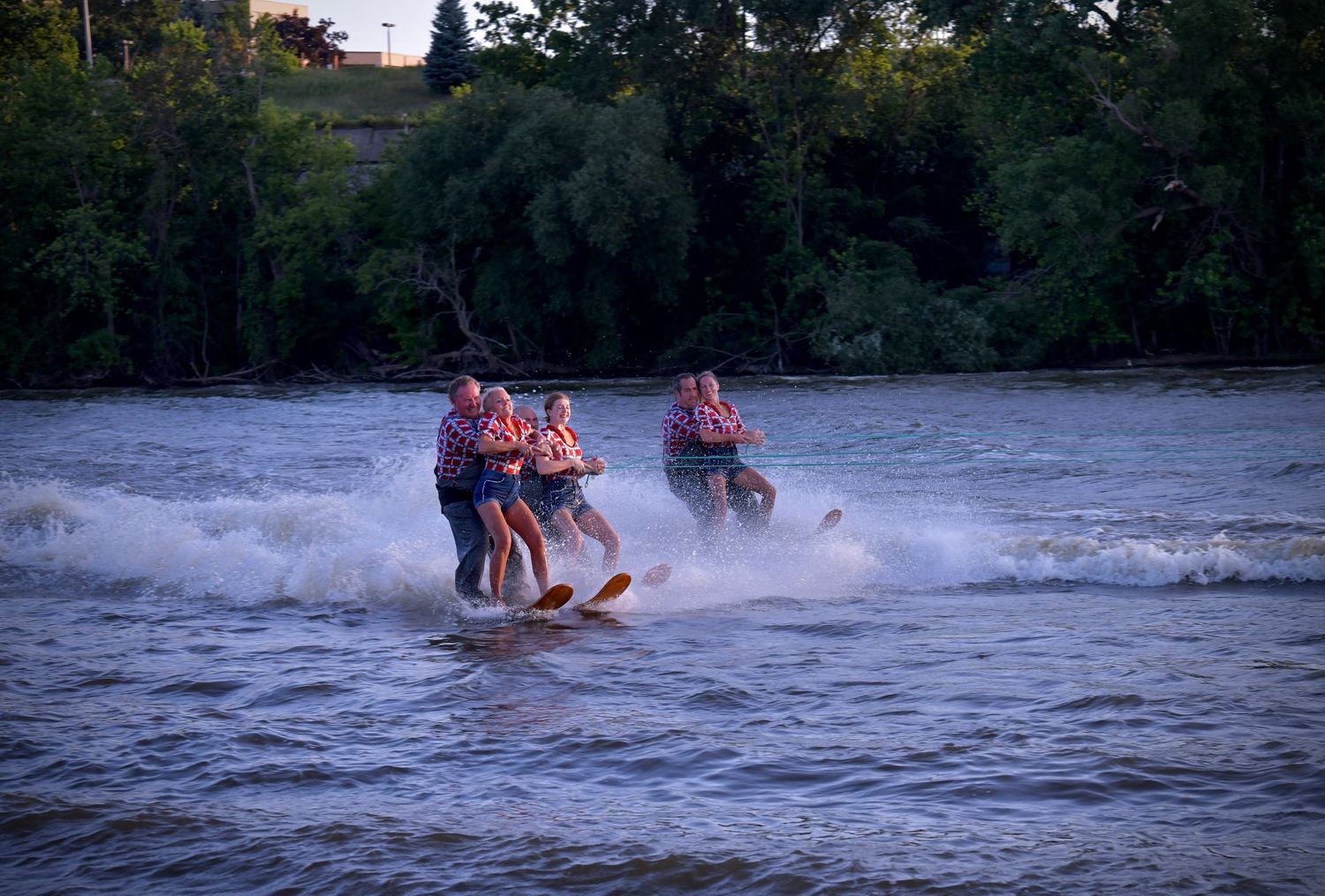 Water skiers wearing bright orange life jackets glide across the water creating spray during an evening ride.