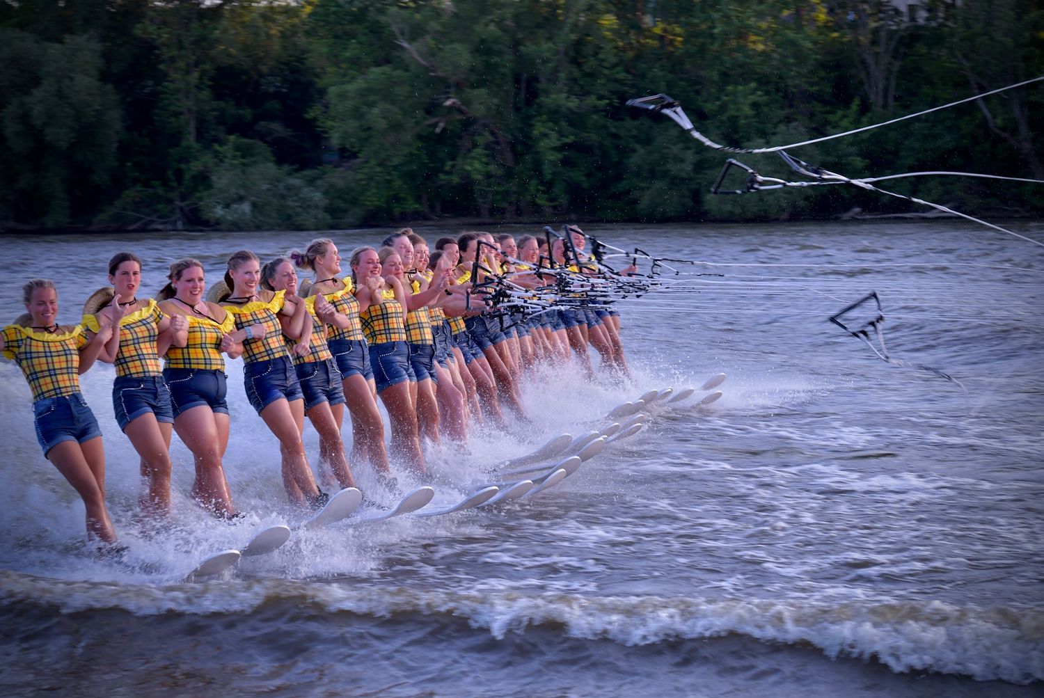 Water skiers form a line holding hands while gliding across the water in synchronized formation during performance.