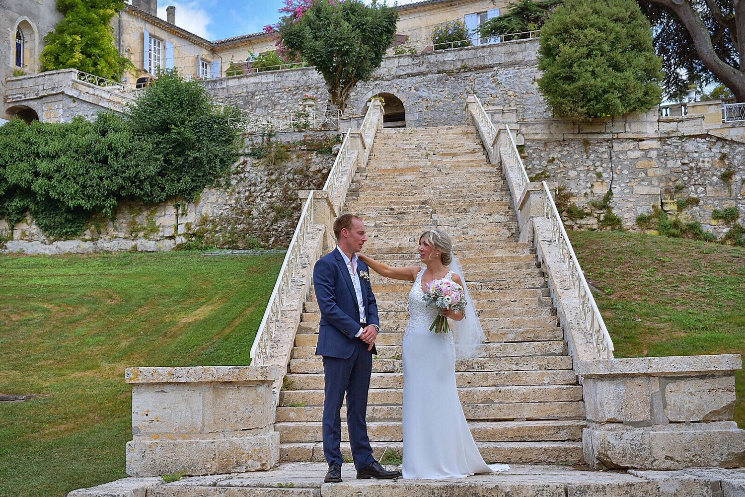 A couple stands together on historic stone steps leading up to an old stone building in a romantic outdoor setting.
