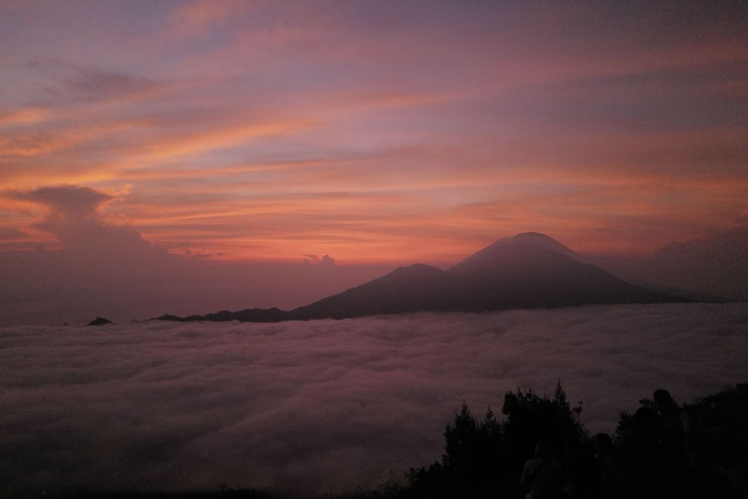 Stunning panorama of Mount Fuji at sunset with dramatic pink and orange clouds rolling across the landscape.