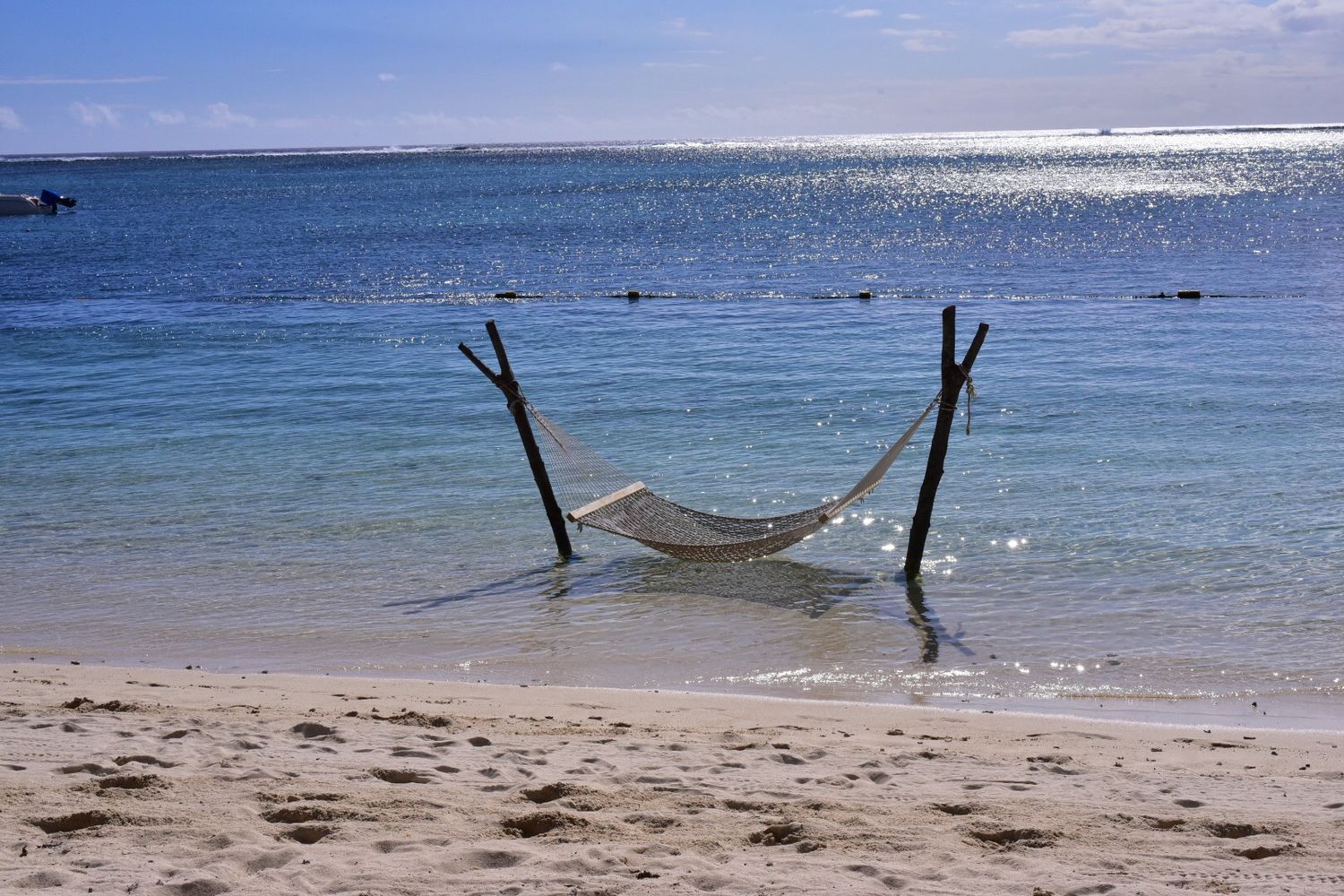 Hammock suspended between wooden posts on a tranquil tropical beach with turquoise water.