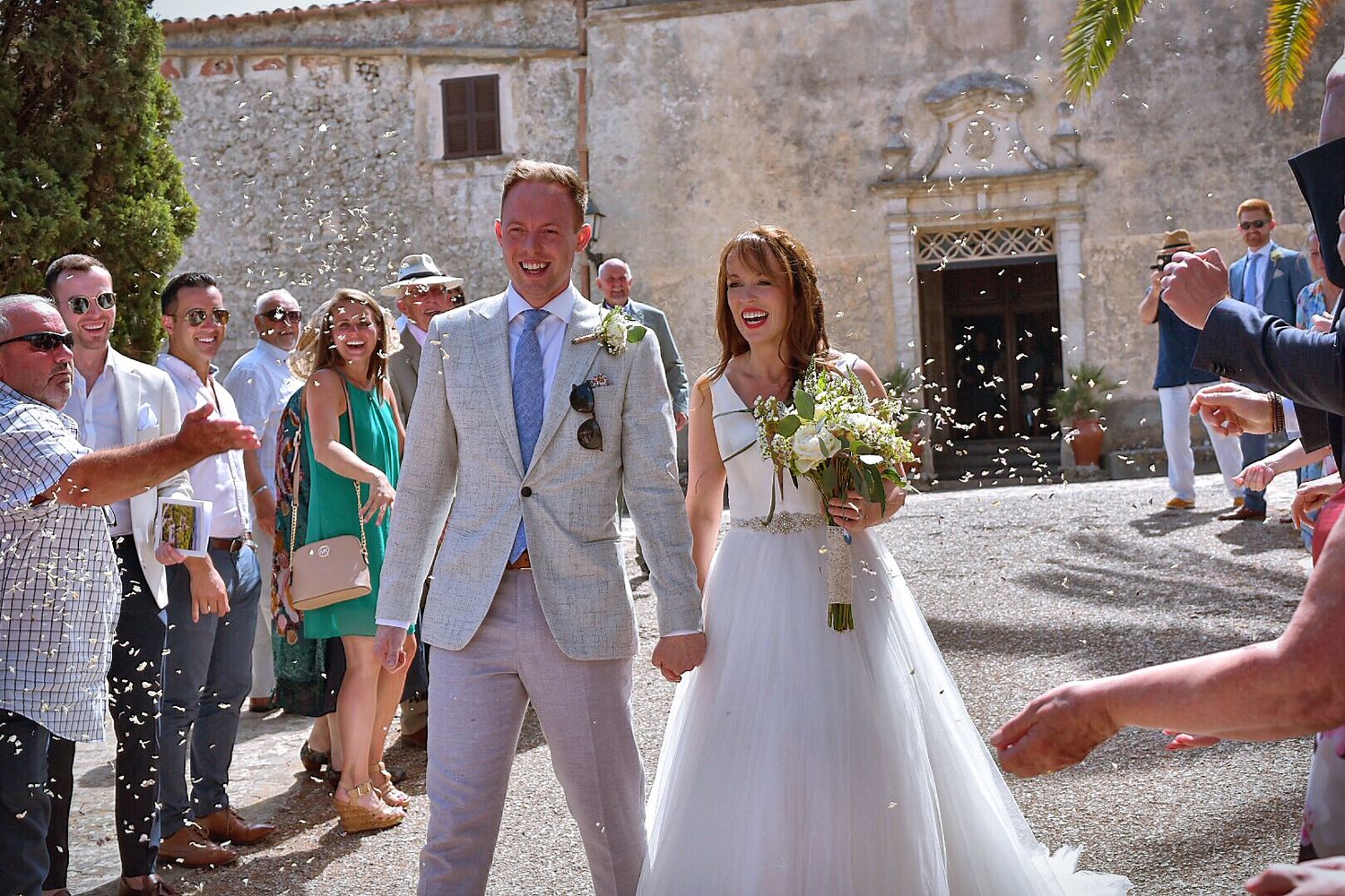 Wedding guests celebrating in an ancient stone courtyard under bright sunlight.