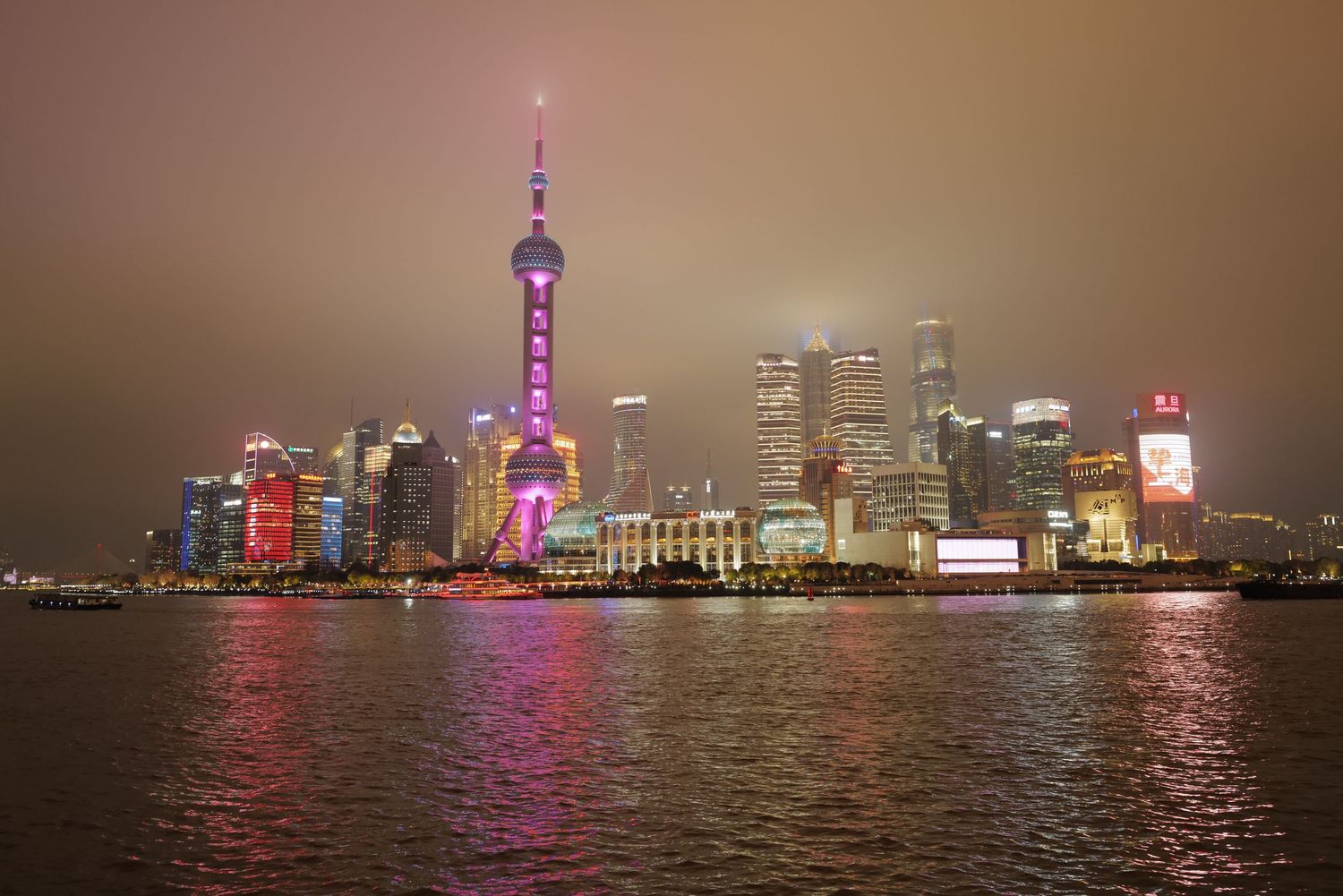 Shanghai's illuminated Pudong skyline at night with Oriental Pearl Tower reflecting on the Huangpu River.