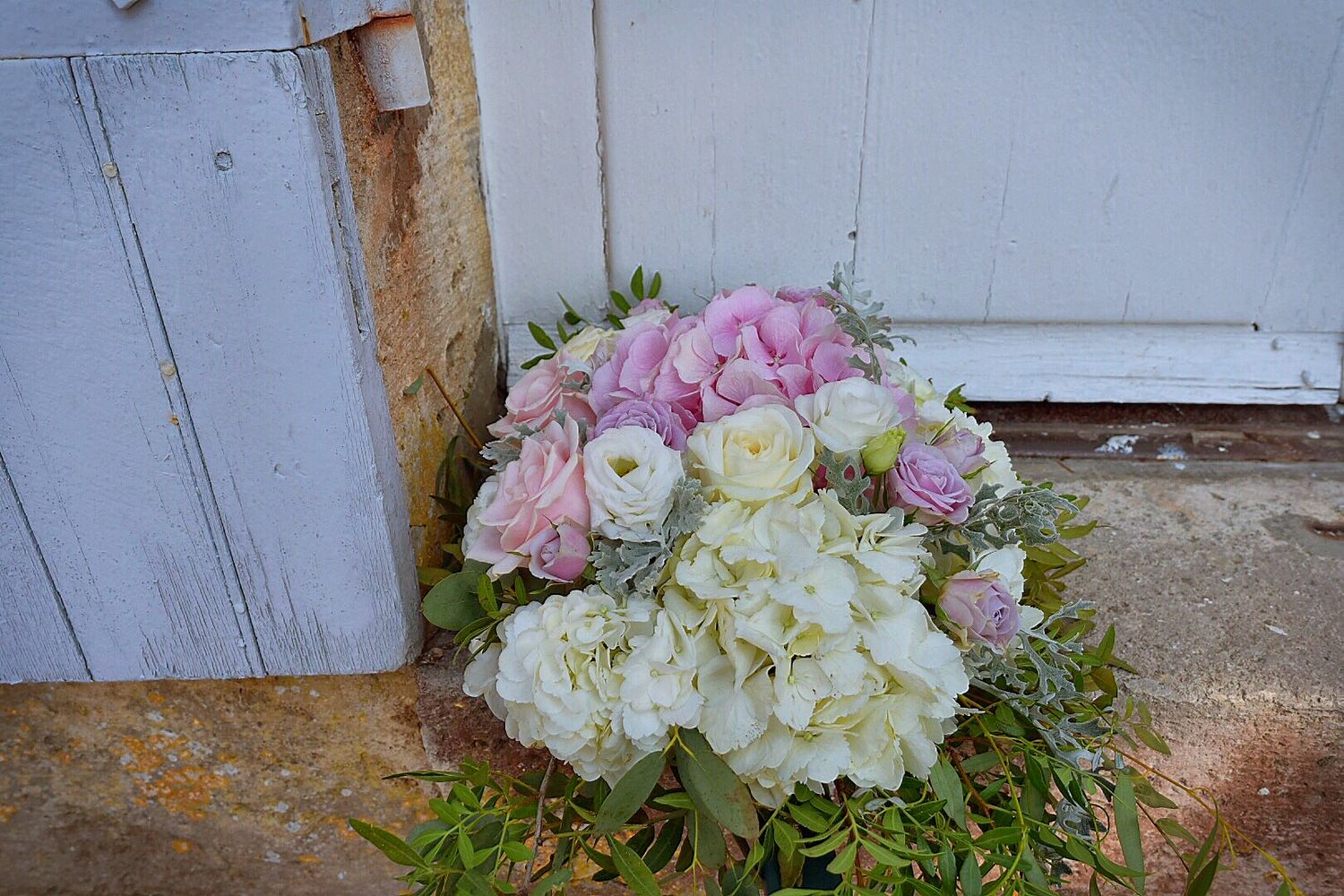 Beautiful bridal bouquet with pink and white hydrangeas resting against rustic white wooden door.