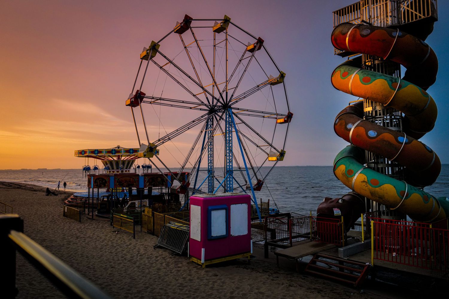 Silhouettes of carnival rides and attractions against a vibrant sunset sky.