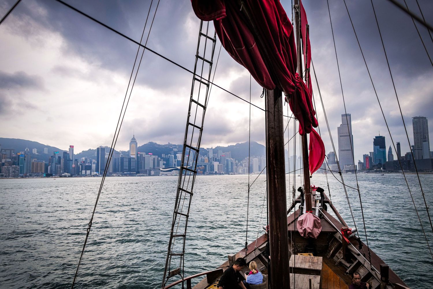 View from traditional junk boat sailing across Victoria Harbor towards Hong Kong skyline.