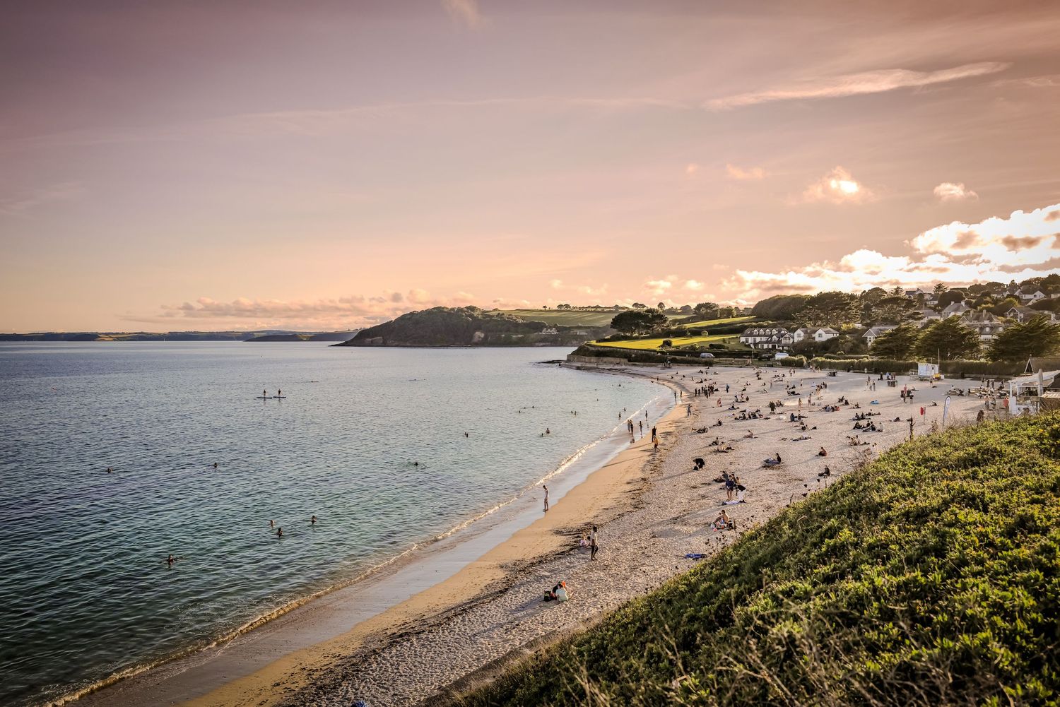 Panoramic view of a sandy beach with people enjoying the ocean at sunset.