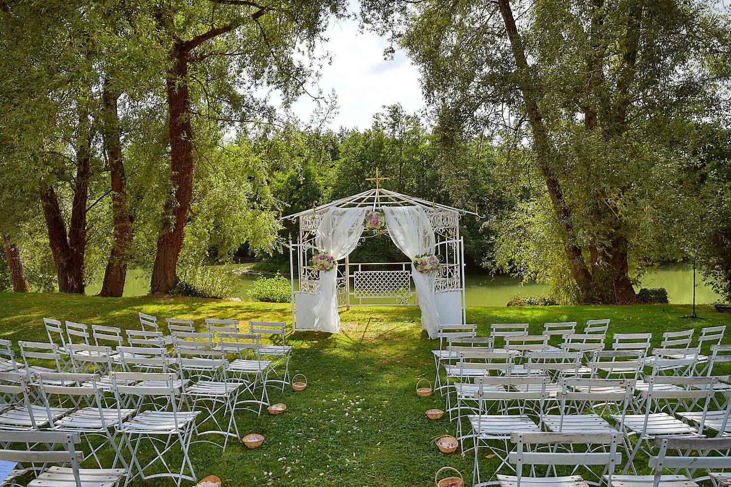 Elegant outdoor wedding ceremony setup with white gazebo and folding chairs arranged on green lawn surrounded by trees.