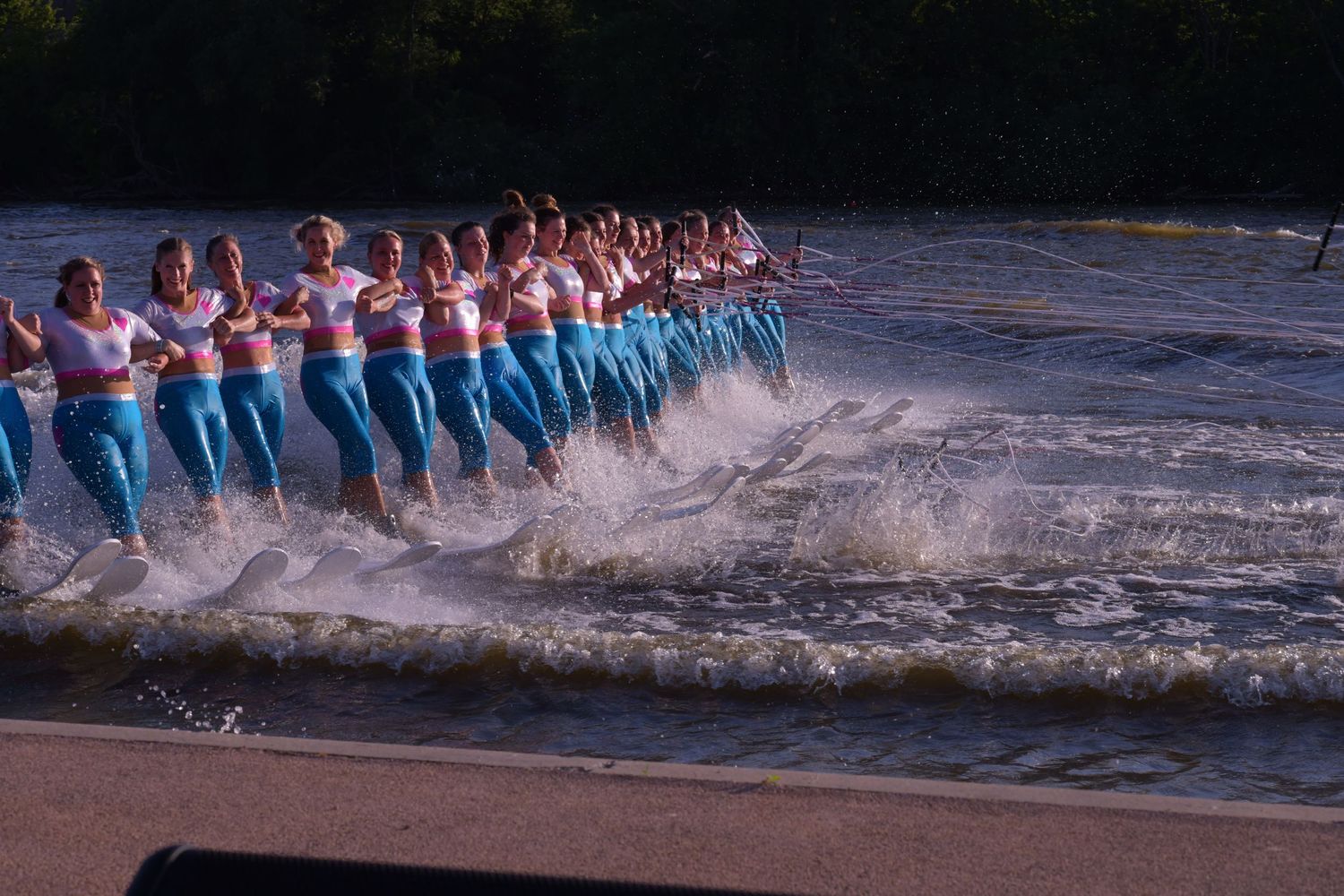 A water skiing team performs a synchronized line formation creating dramatic splashes on a lake.