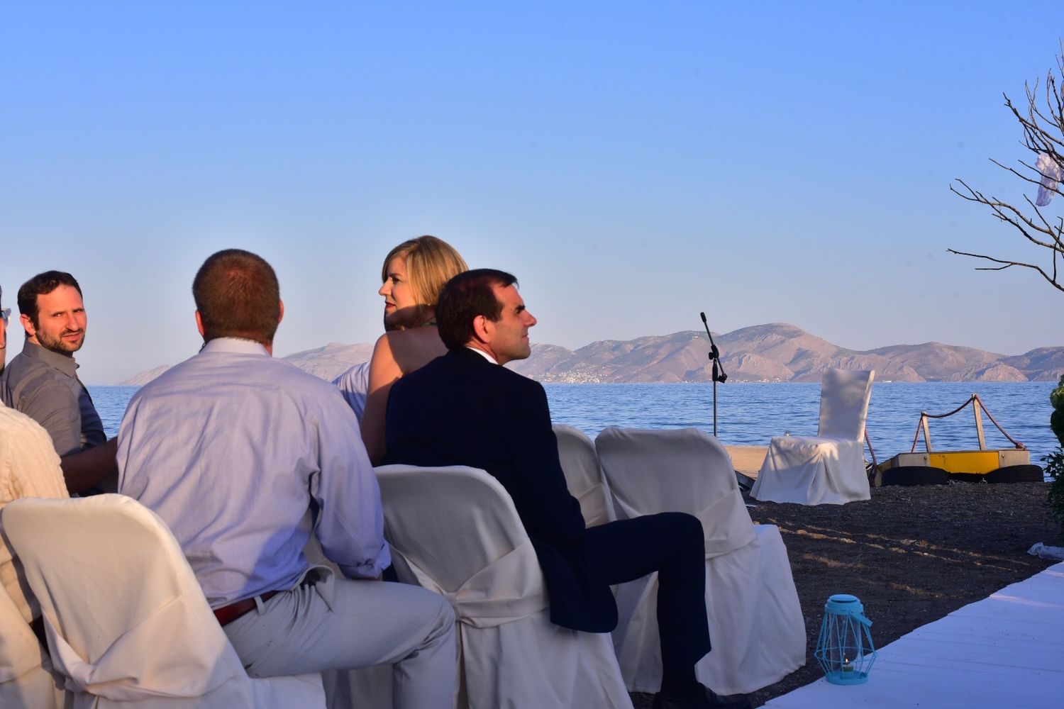 Guests seated at an oceanfront wedding ceremony with mountains visible in the background.