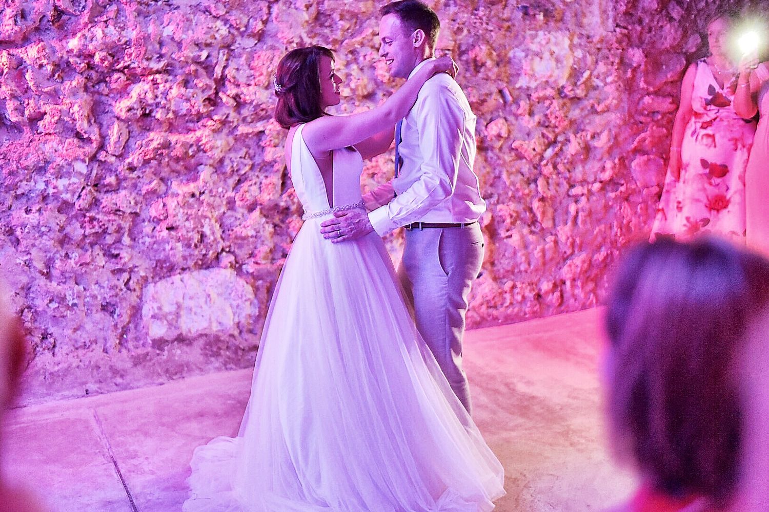 Wedding dance floor illuminated with dramatic purple lighting and stone wall backdrop.