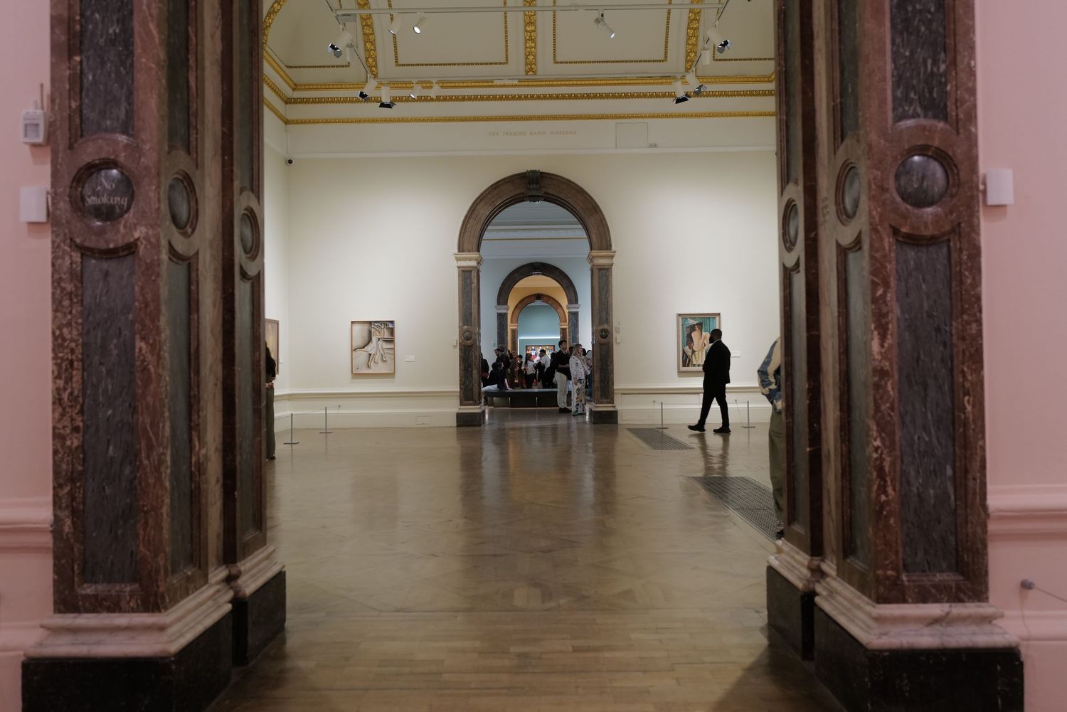 Long museum corridor with ornate wooden doorways and white walls showing artwork displays in the distance.