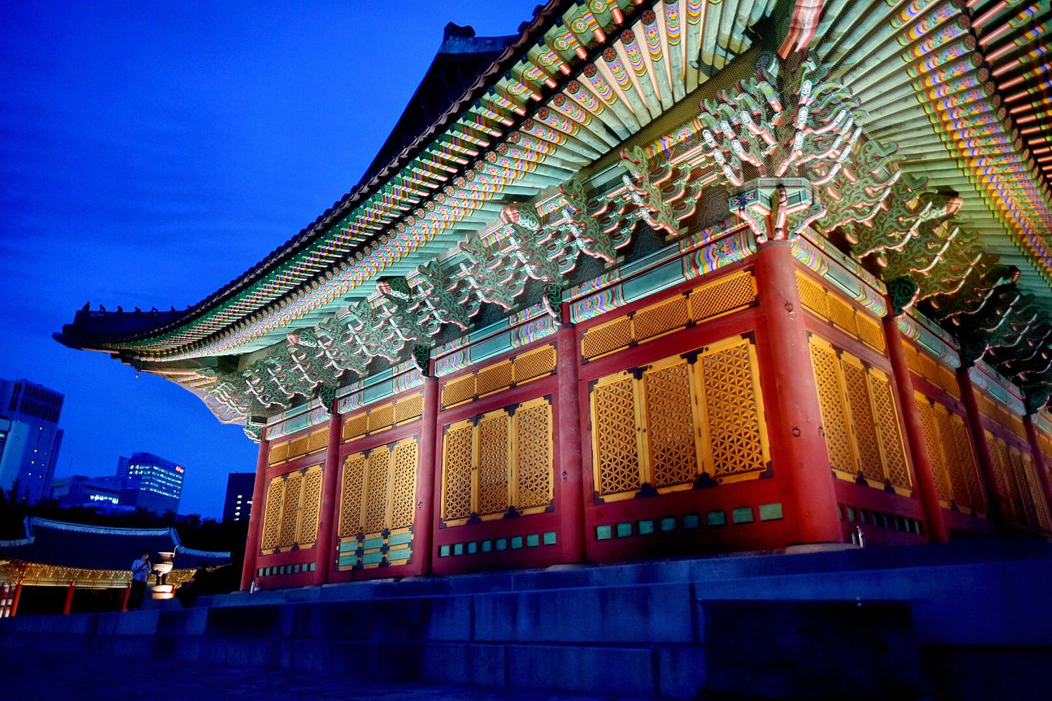 Traditional Korean temple with ornate red and gold roof details glowing against deep blue twilight sky.