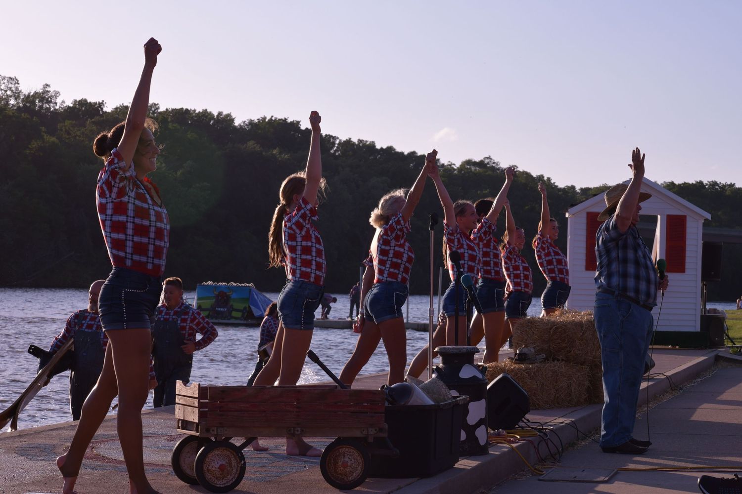 A group of silhouetted people gathered along a waterfront at sunset pulling wagons and enjoying the evening.