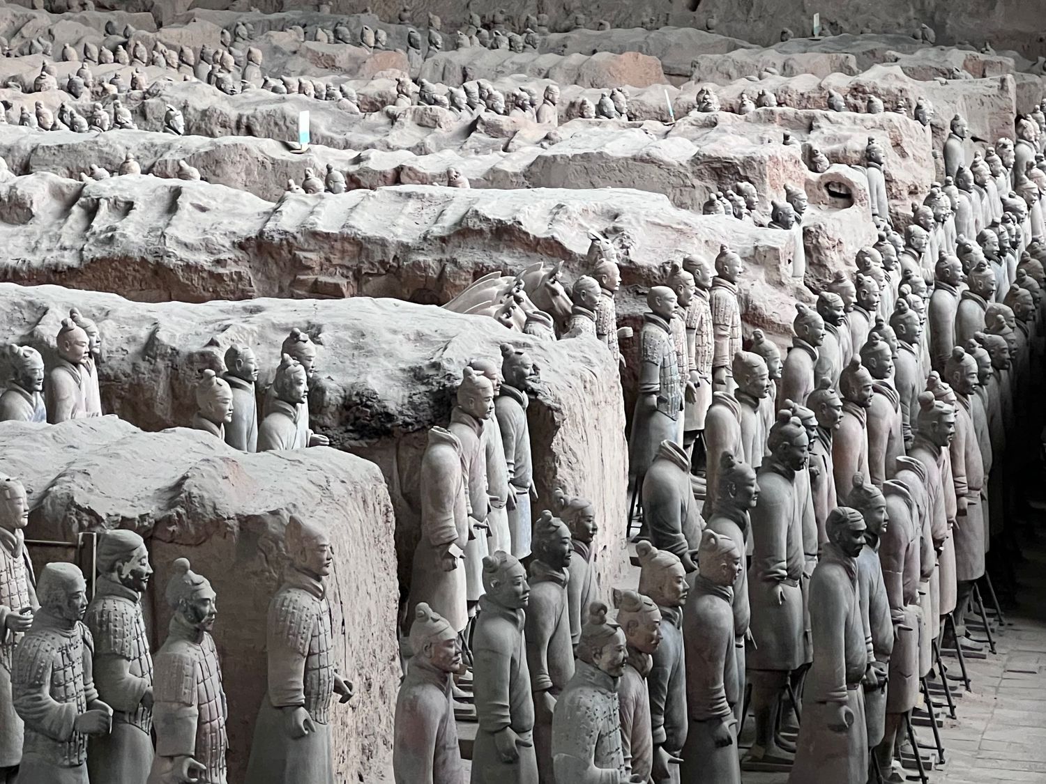 Ancient terracotta army warriors arranged in neat rows within an excavation pit.