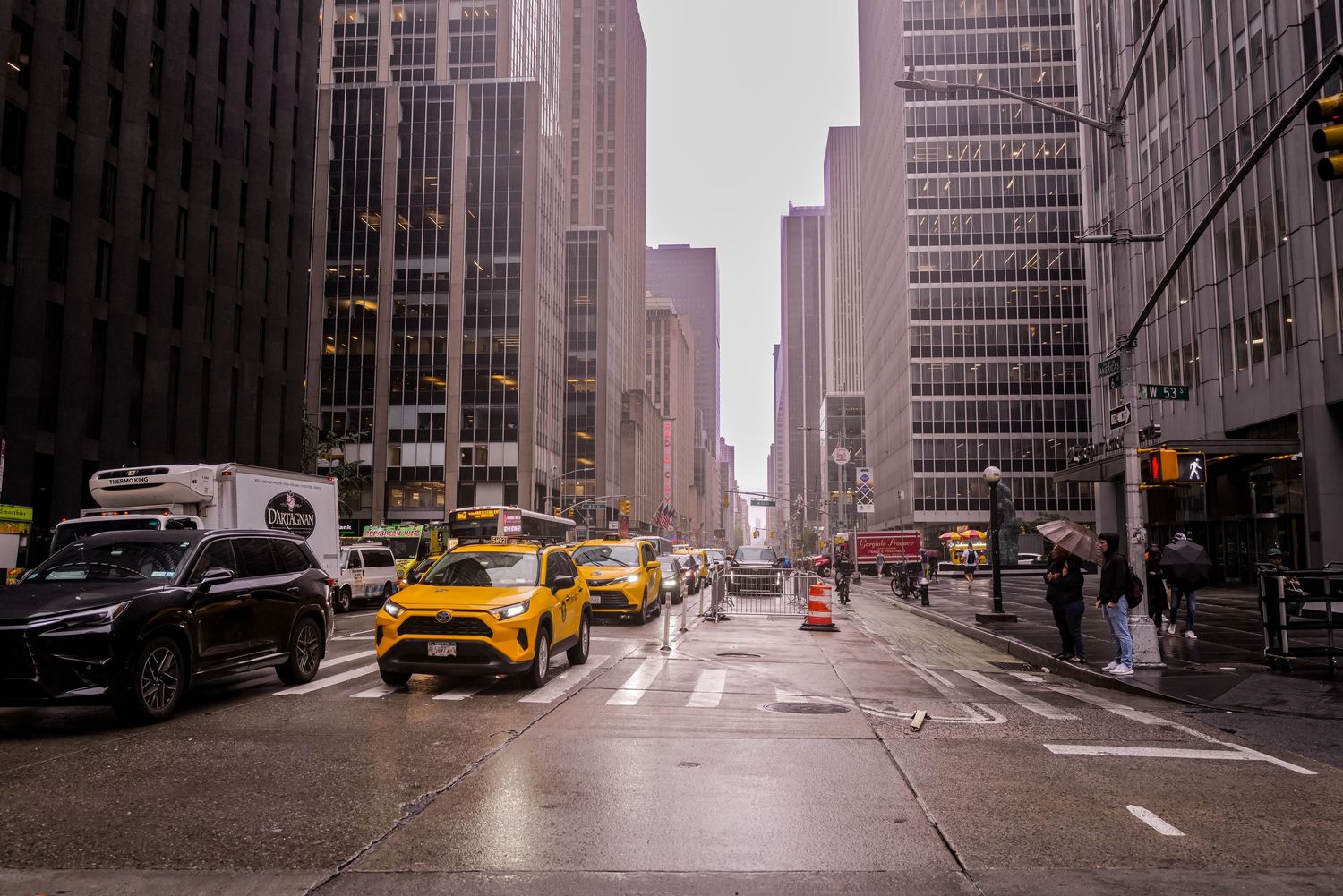 Rainy street scene in Manhattan with yellow taxis and towering skyscrapers.