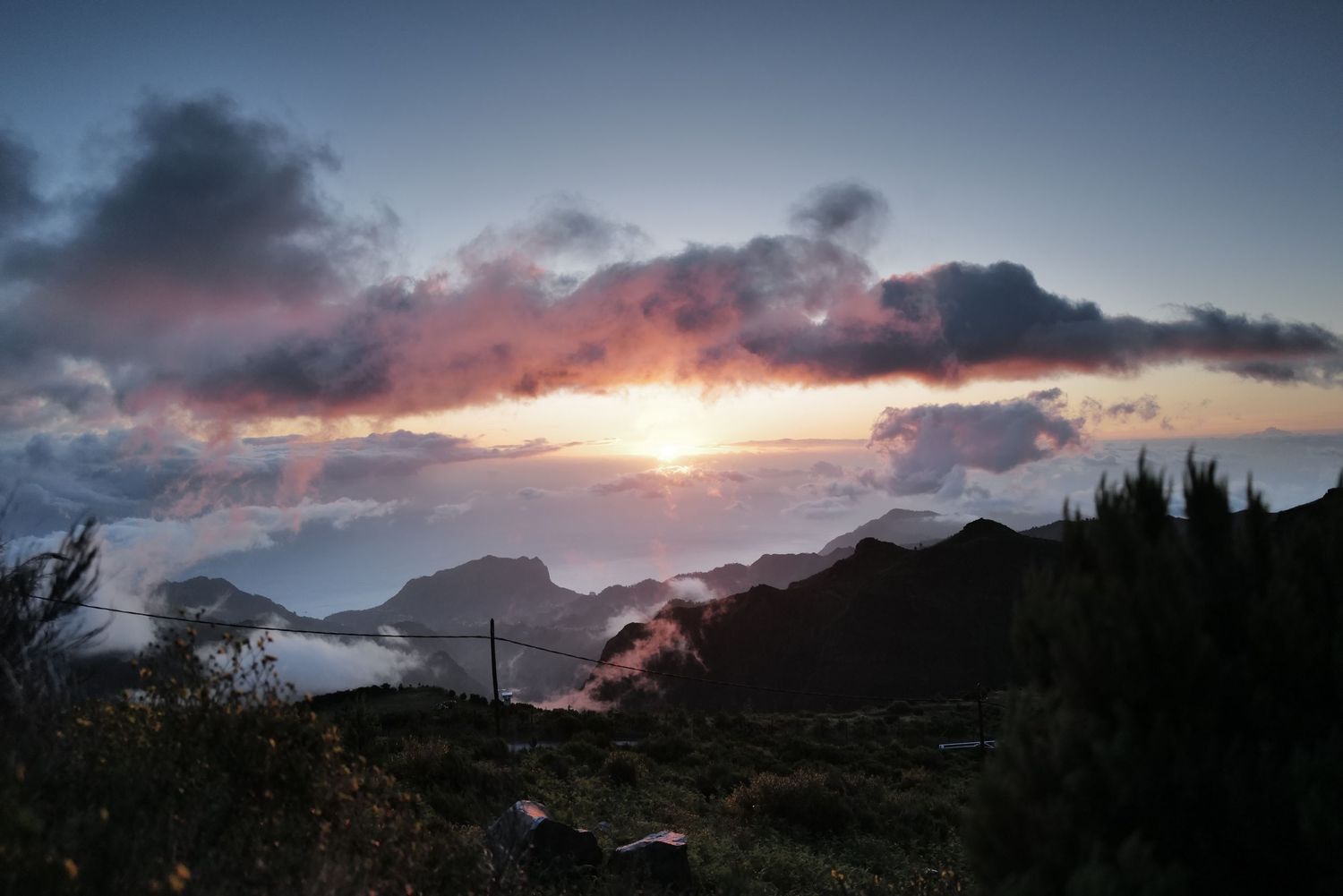 Mountain silhouettes against a colorful sunset sky with dramatic cloud formations.