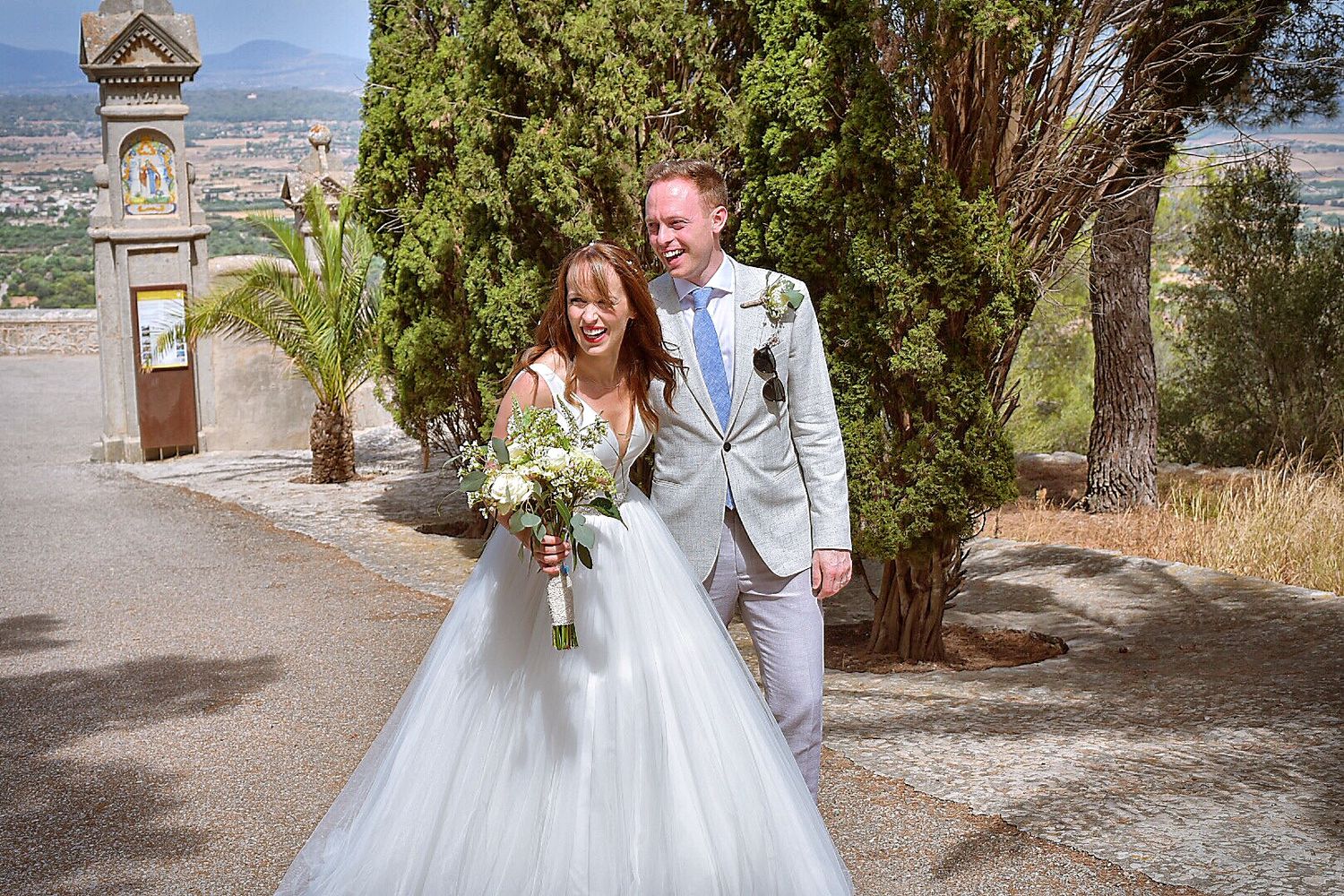 Wedding ceremony taking place in a scenic Mediterranean location with stone architecture and cypress trees.