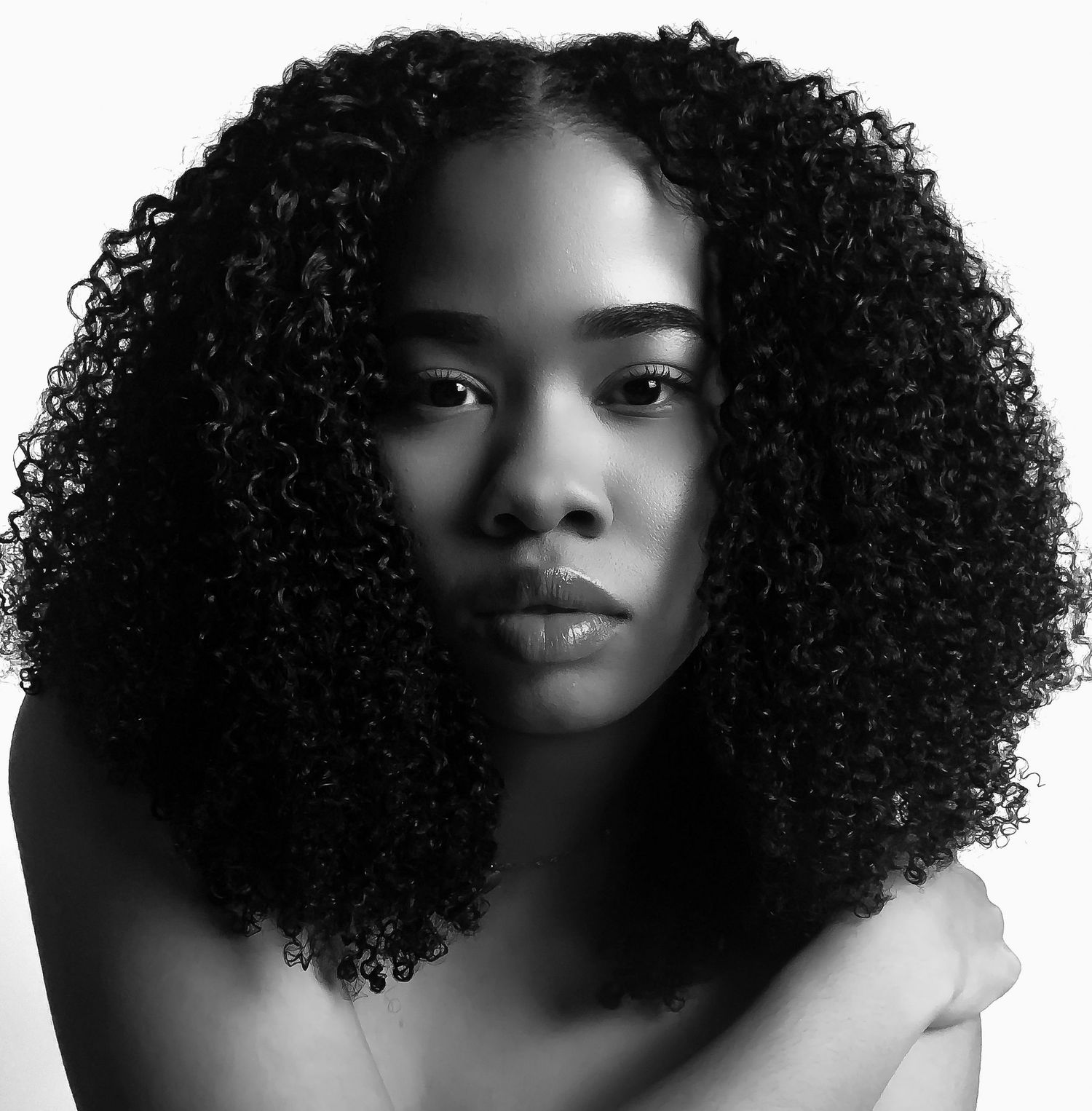 Black and white portrait of a young woman with voluminous natural curly hair against a white background.