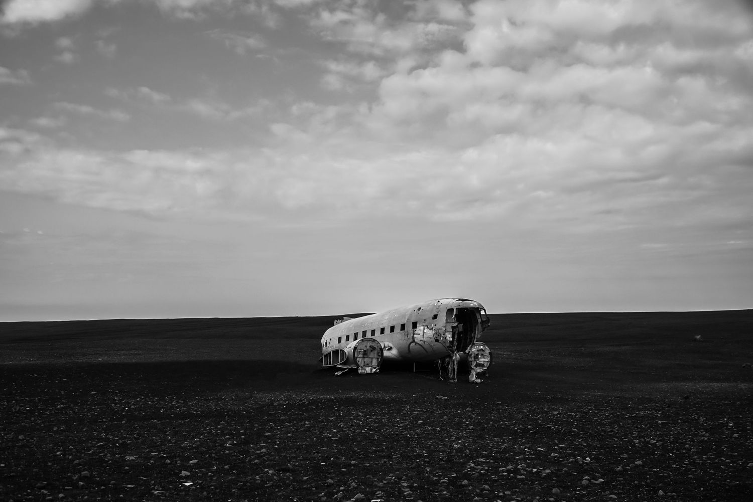 Black and white photo of a plane wreck on a dark volcanic beach under cloudy skies in Iceland.